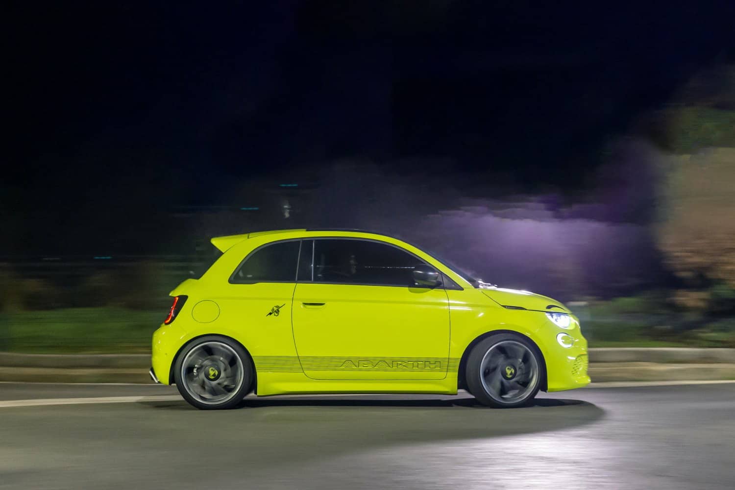 Abarth 500e capturado en acción durante la noche, resaltando su línea lateral y las luces.