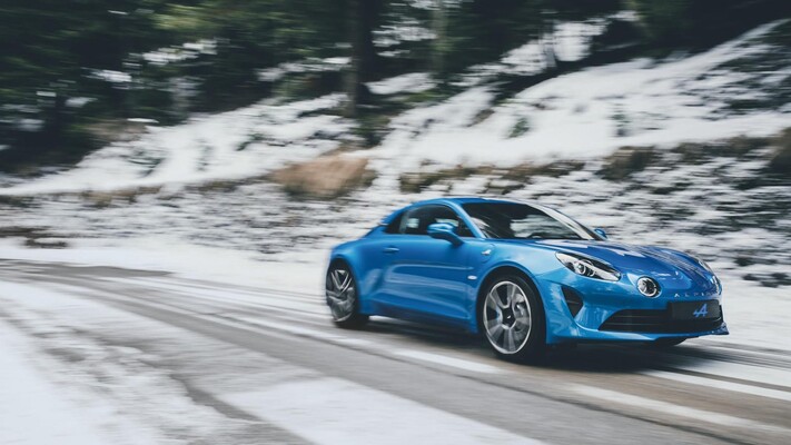 El Alpine A110, azul brillante, capturado deslizándose ágilmente por una carretera nevada.