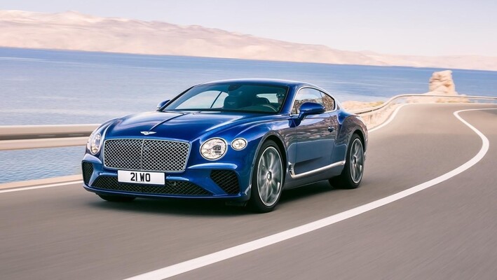 Bentley Continental GT en azul recorriendo costa soleada.