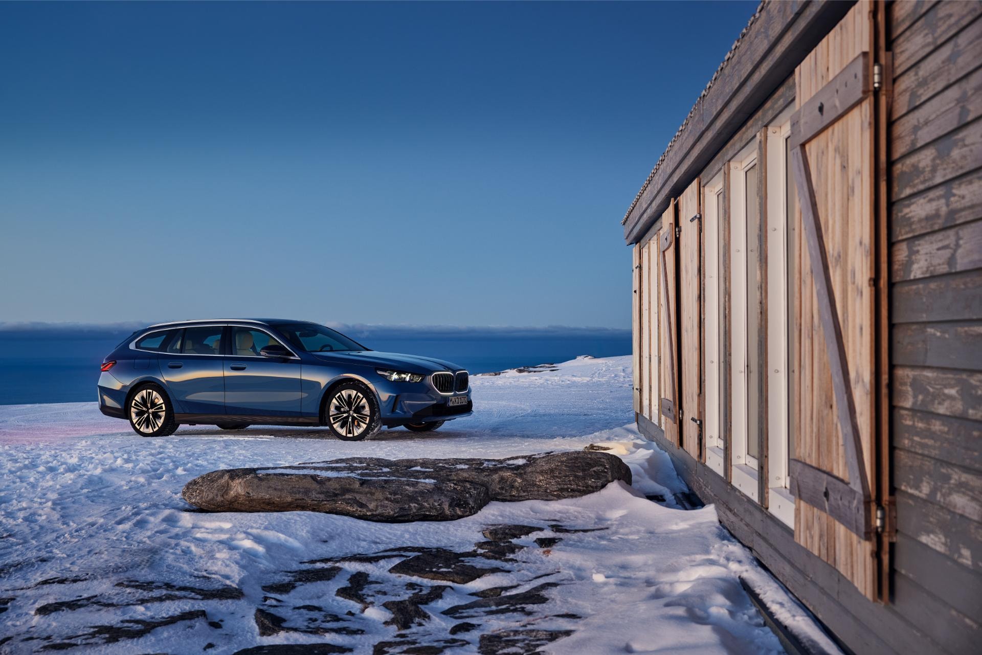 Vista lateral del BMW Serie 5 Touring estacionado junto a una casa de madera.