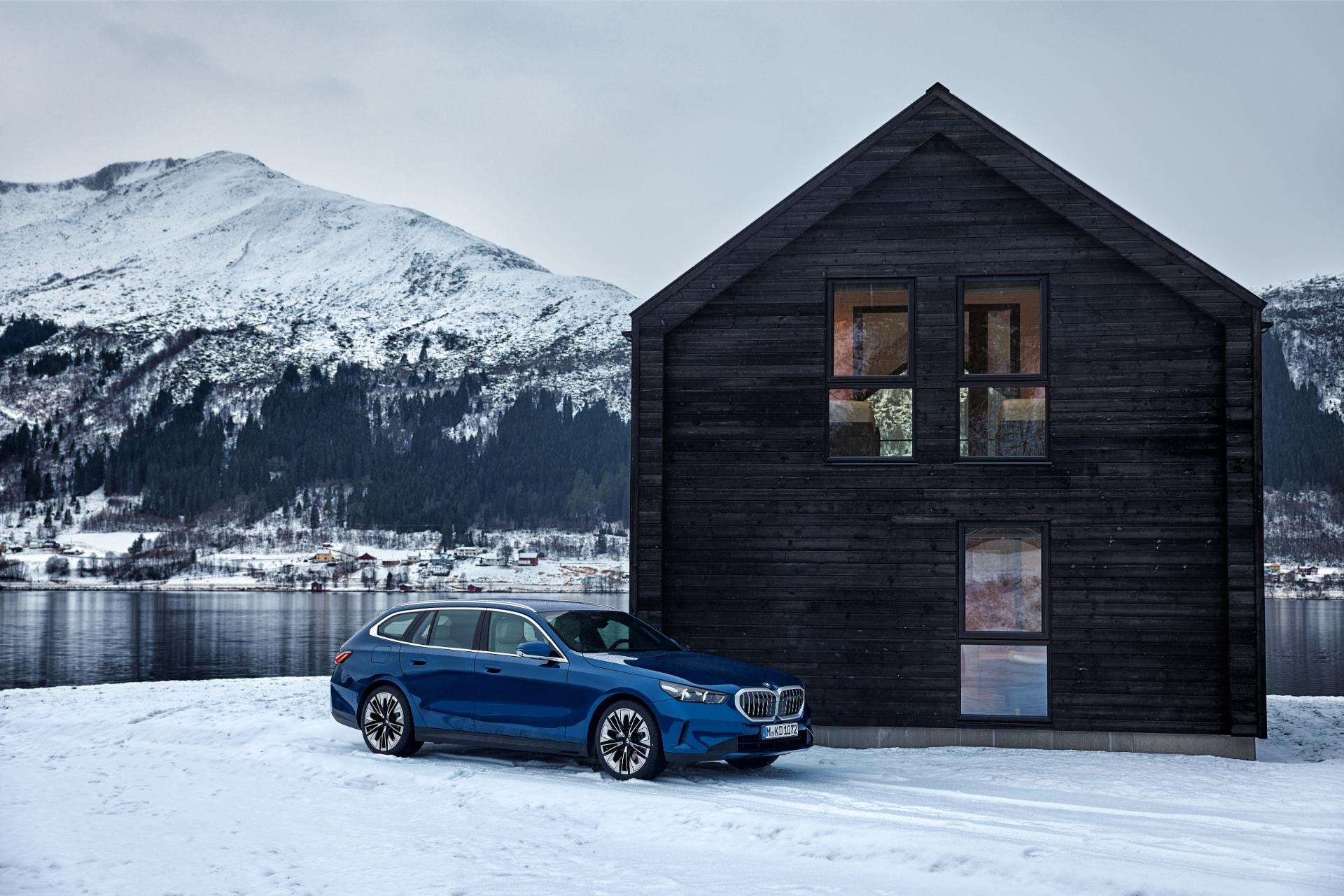 Lateral del BMW Serie 5 frente a cabaña con montañas nevadas.