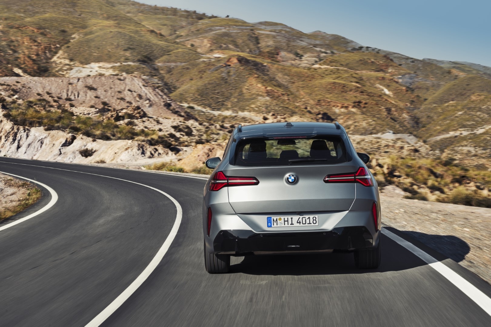 Vista trasera del BMW X3 tomando una curva en carretera de montaña.