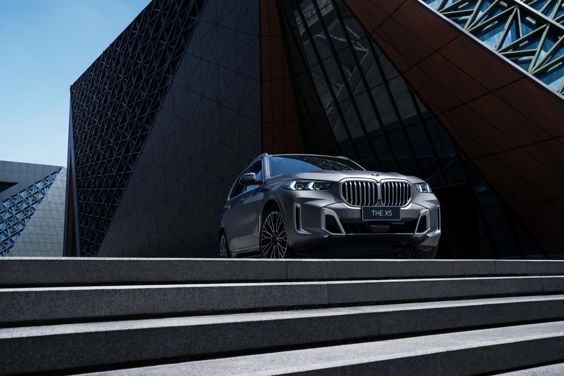 BMW X5 Híbrido posicionado frente a una arquitectura geométrica, enfocando su frontal.