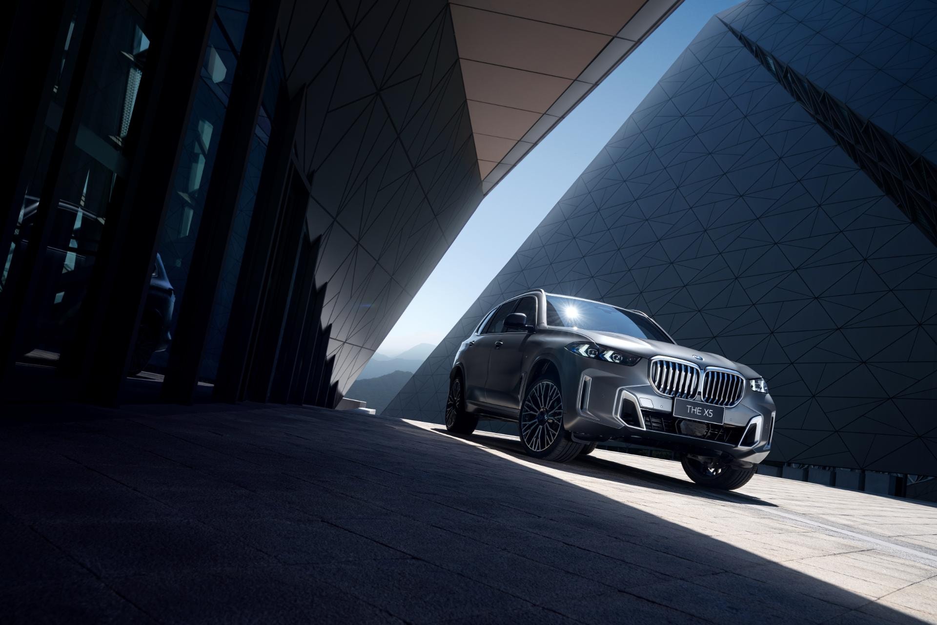 BMW X5 Híbrido mostrando su frontal y lateral con una fachada moderna de fondo.