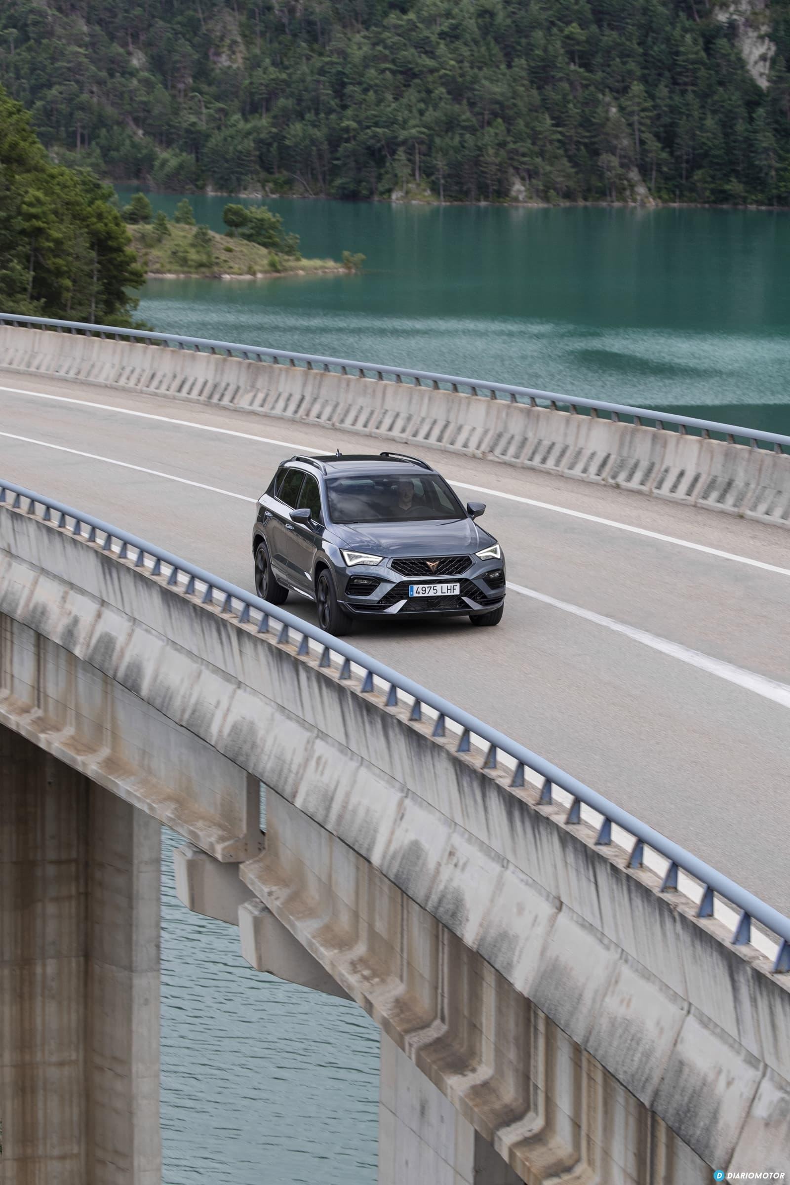 Cupra Ateca en conducción sobre puente con lago, resaltando su diseño lateral.