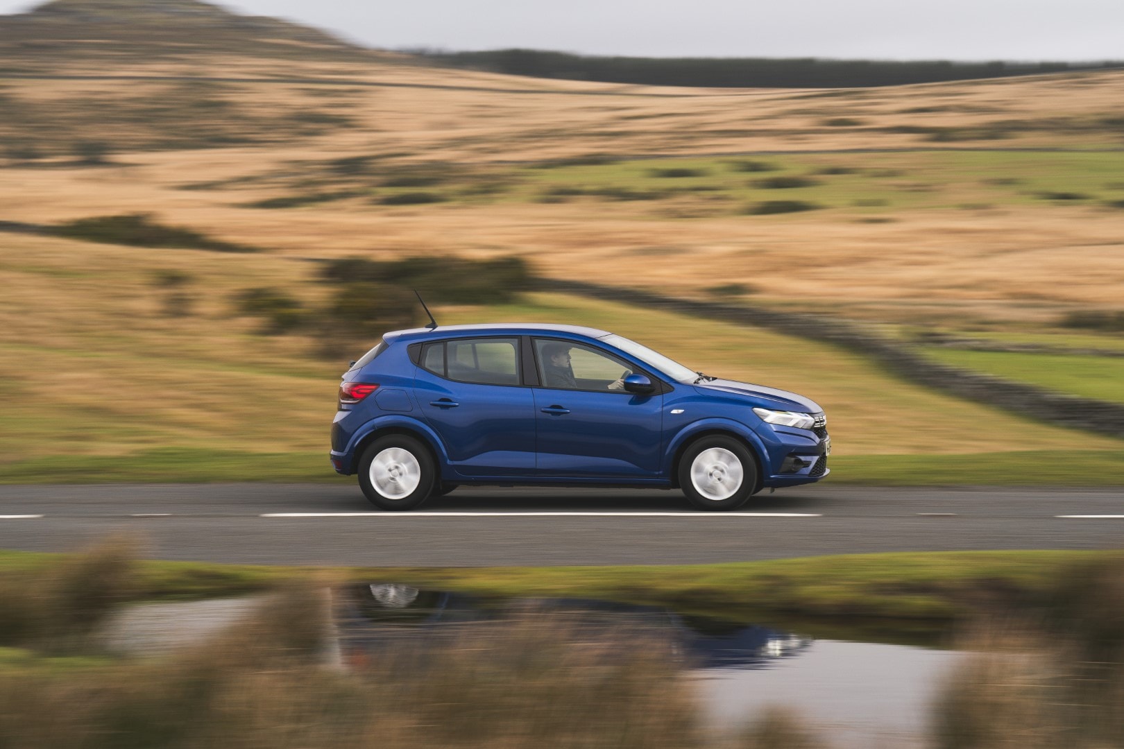 Imagen lateral del Dacia Sandero en movimiento con un paisaje borroso.