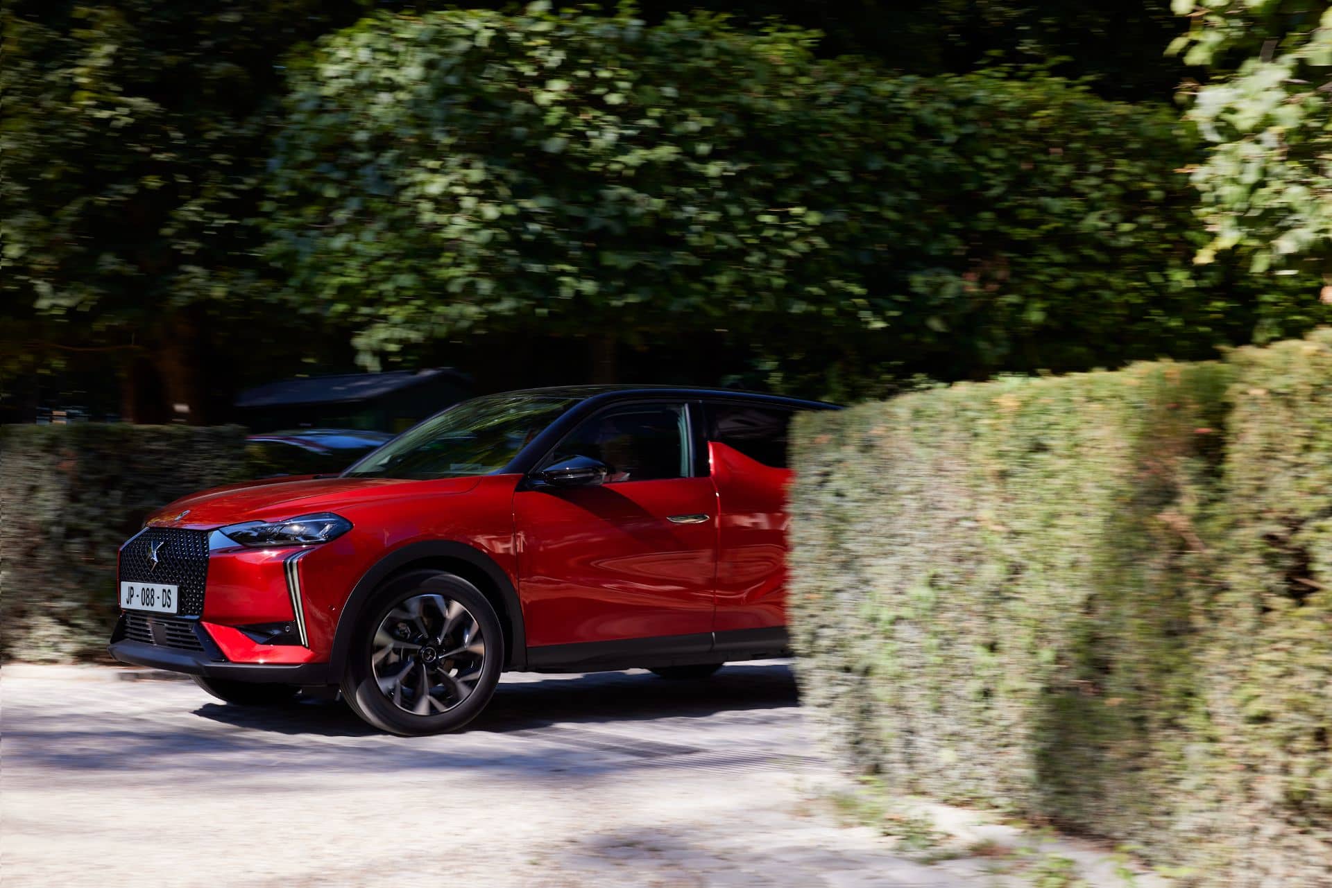 Vista lateral del DS 3 en movimiento por un camino arbolado.