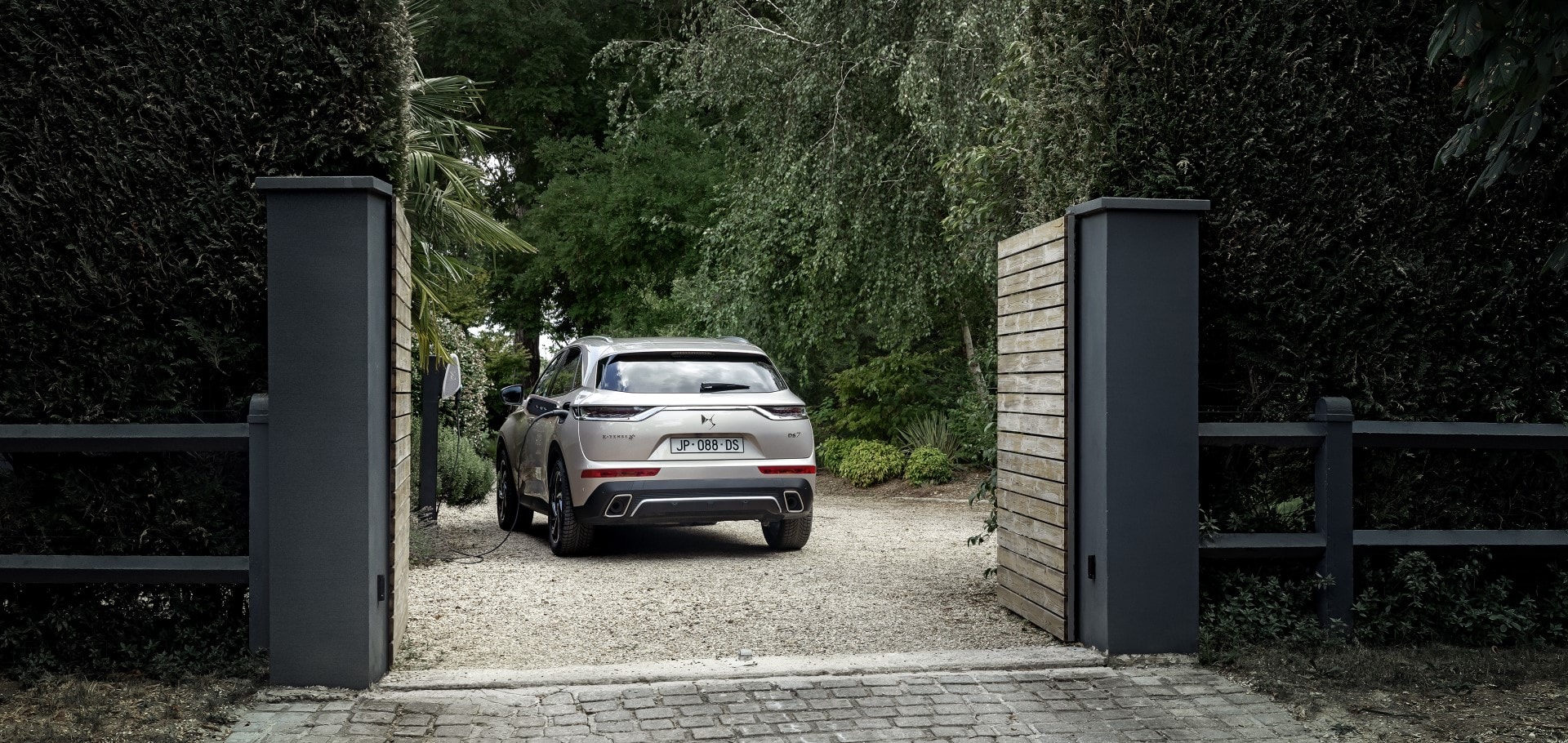 Vista trasera del DS7 Híbrido entrando a un área residencial privada, exhibiendo su línea trasera.