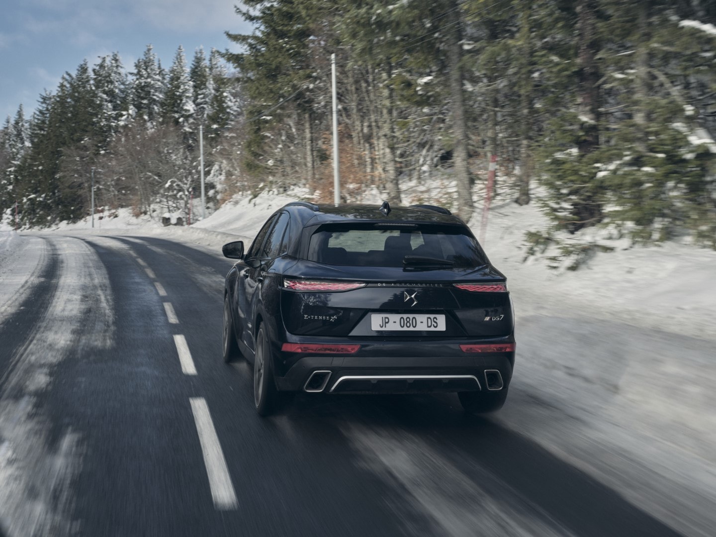 Vista trasera del DS7 Híbrido en movimiento, enfatizando su diseño trasero y dualidad de escapes.