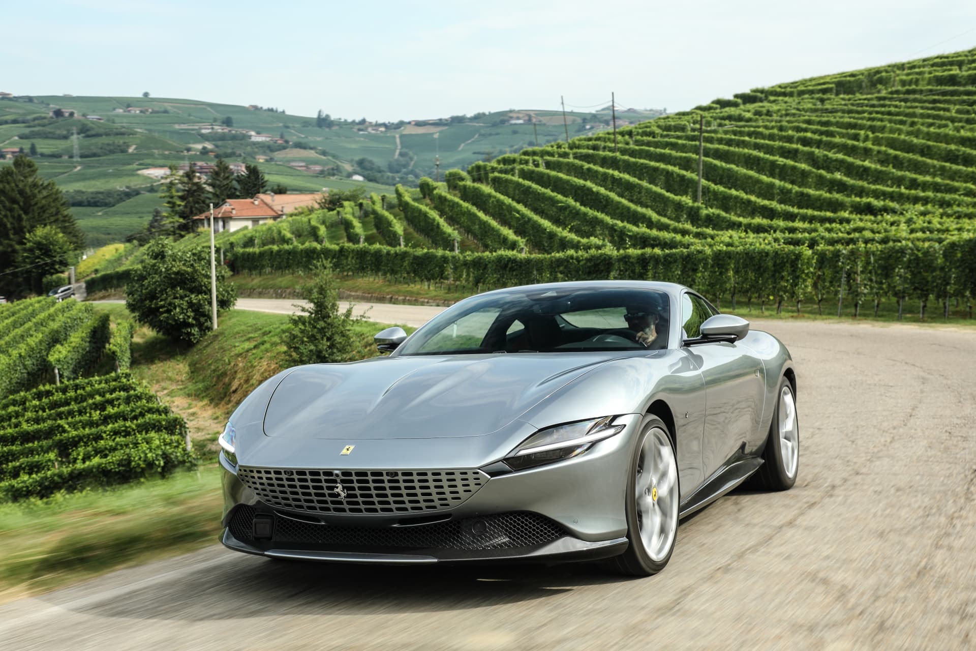 Vista delantera y lateral del Ferrari Roma en carretera con viñedos de fondo