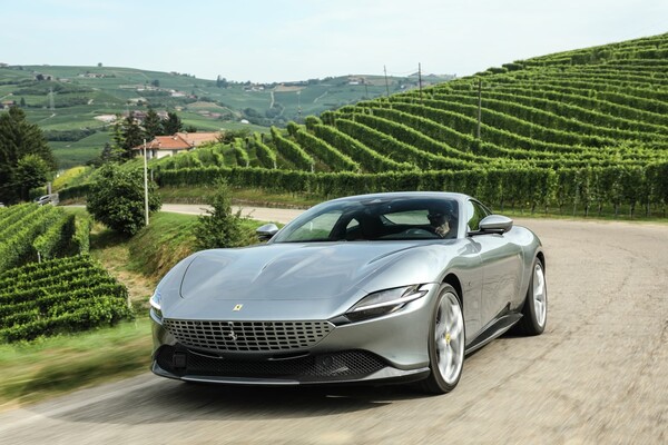 Vista delantera y lateral del Ferrari Roma en carretera con viñedos de fondo Vista delantera y lateral del Ferrari Roma en carretera con viñedos de fondo