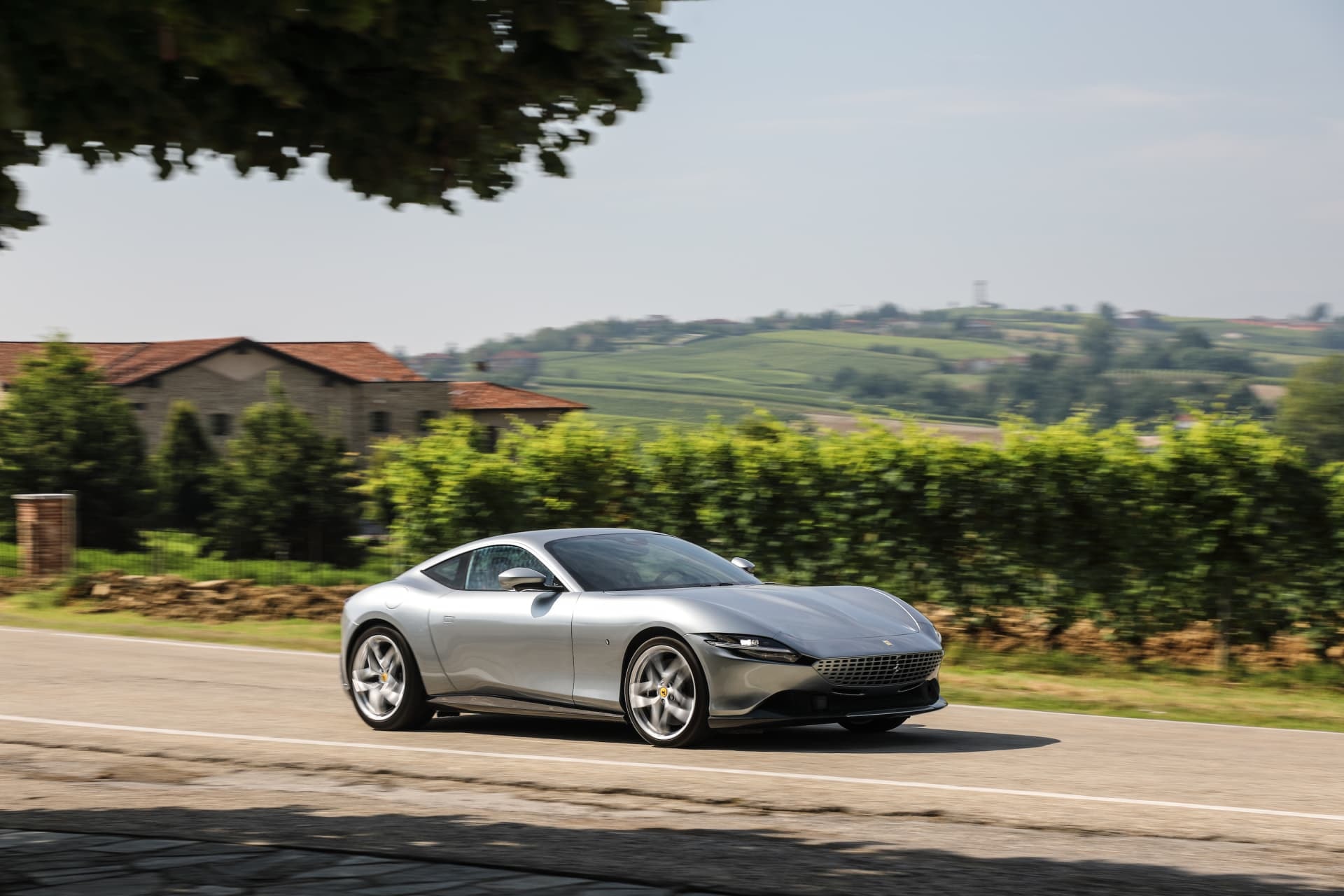 Ferrari Roma en movimiento frente a un contexto rural tranquilo.