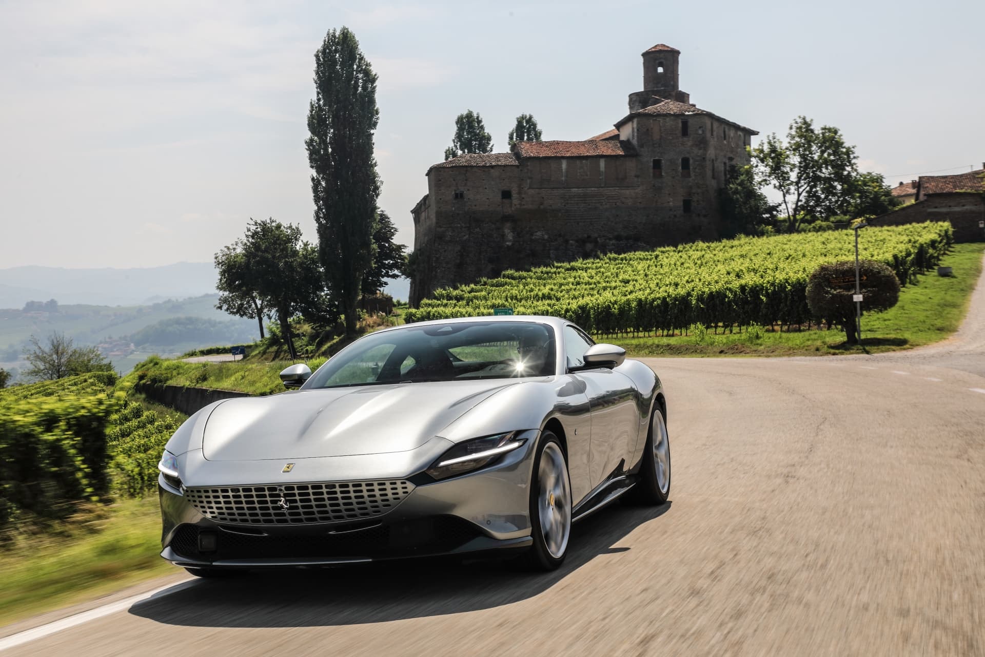 Ferrari Roma avanzando con castillo de fondo, combina diseño y tradición.