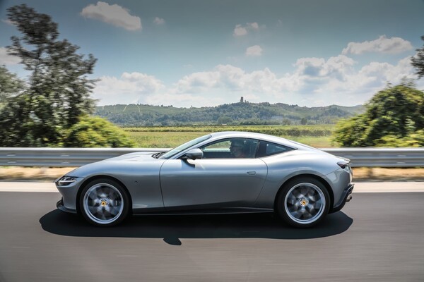 Perfil dinámico del Ferrari Roma rodando por carretera con paisaje verde Perfil dinámico del Ferrari Roma rodando por carretera con paisaje verde