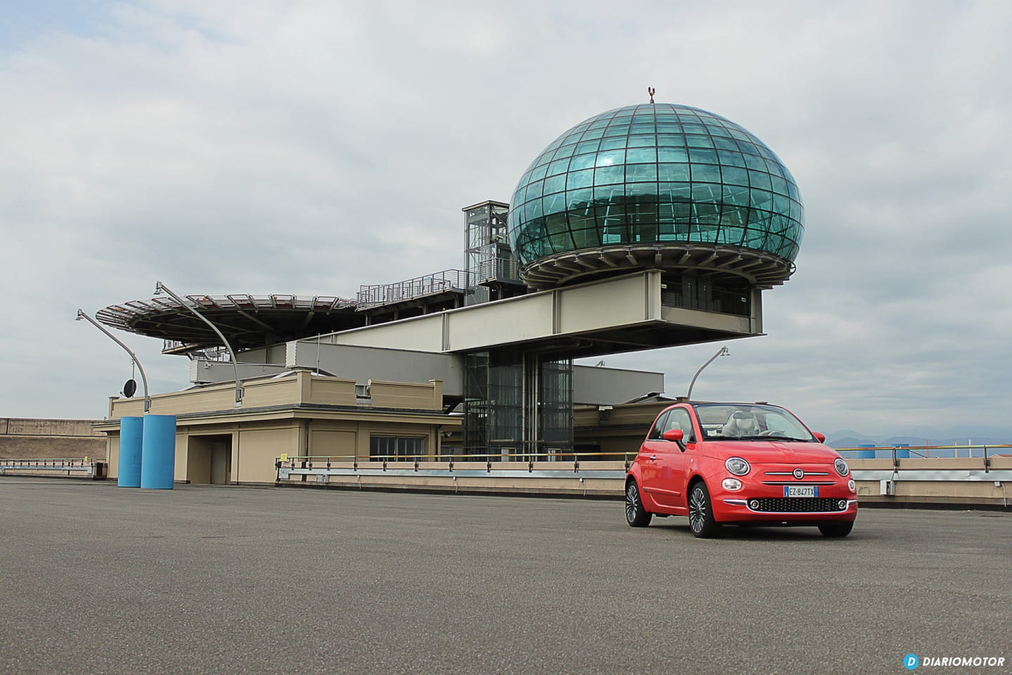 Fiat 500 rojo posado frente a una construcción de cristal, demostrando su estilo urbanita.