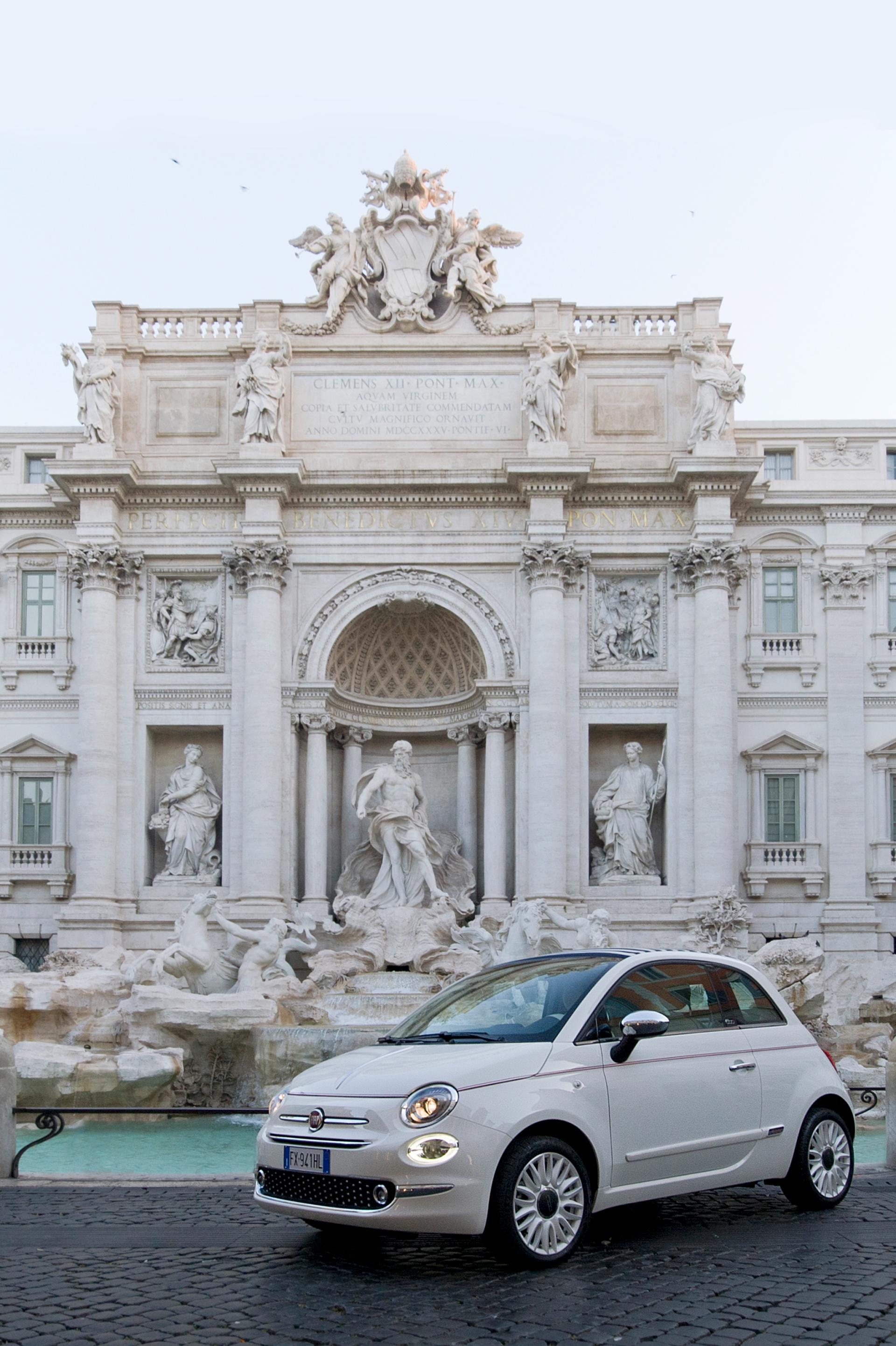 Fiat 500C blanco posando ante la Fontana di Trevi, un marco histórico para un diseño atemporal.