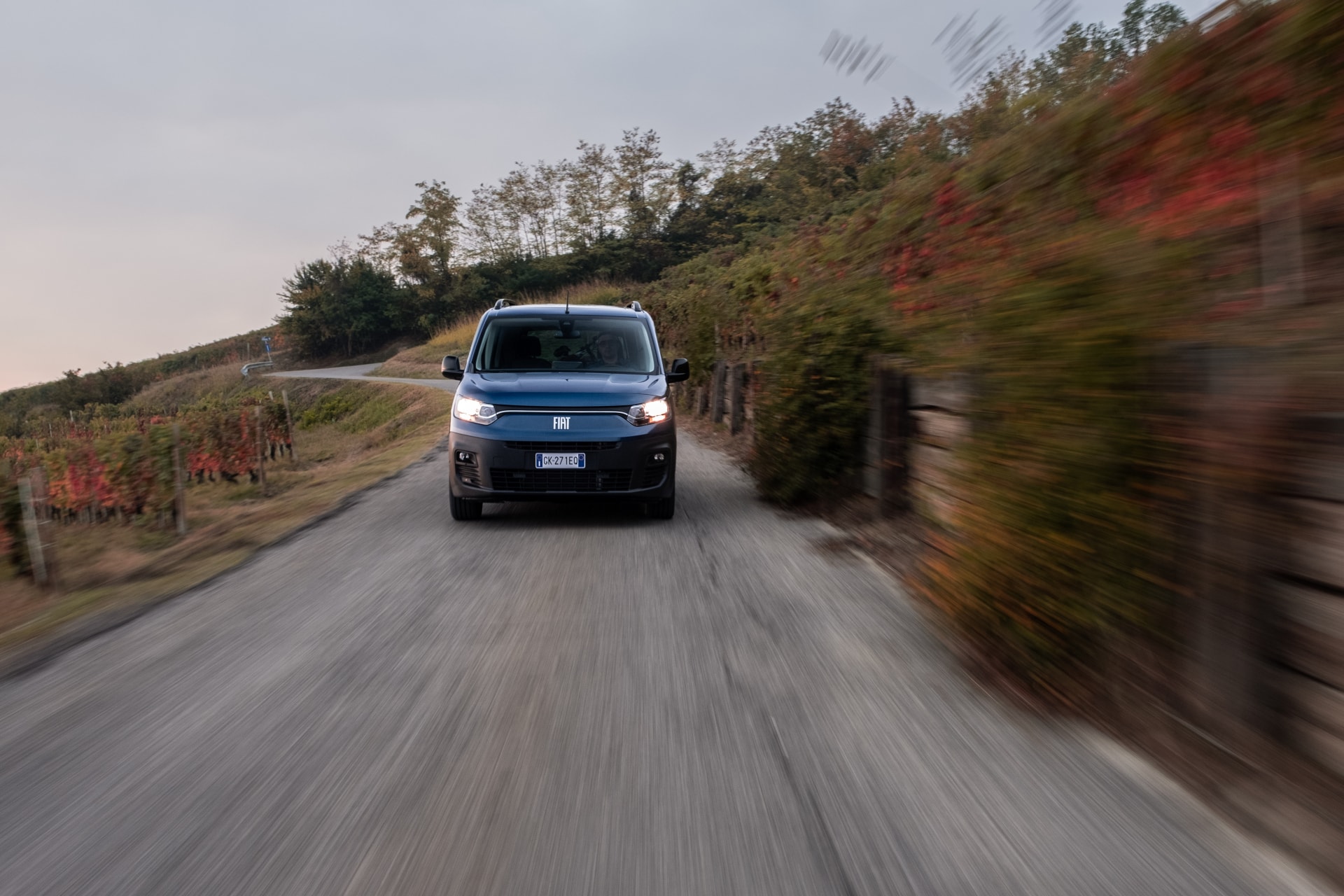 Perspectiva frontal y lateral del Fiat Doblò eléctrico en movimiento por carreteras rurales.