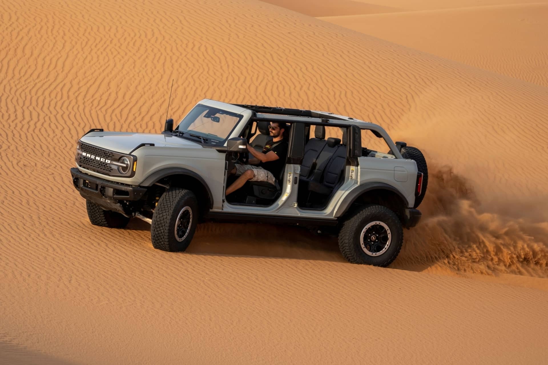 Un Ford Bronco sin techo ni puertas atravesando dunas de arena, perfecto para aventureros.
