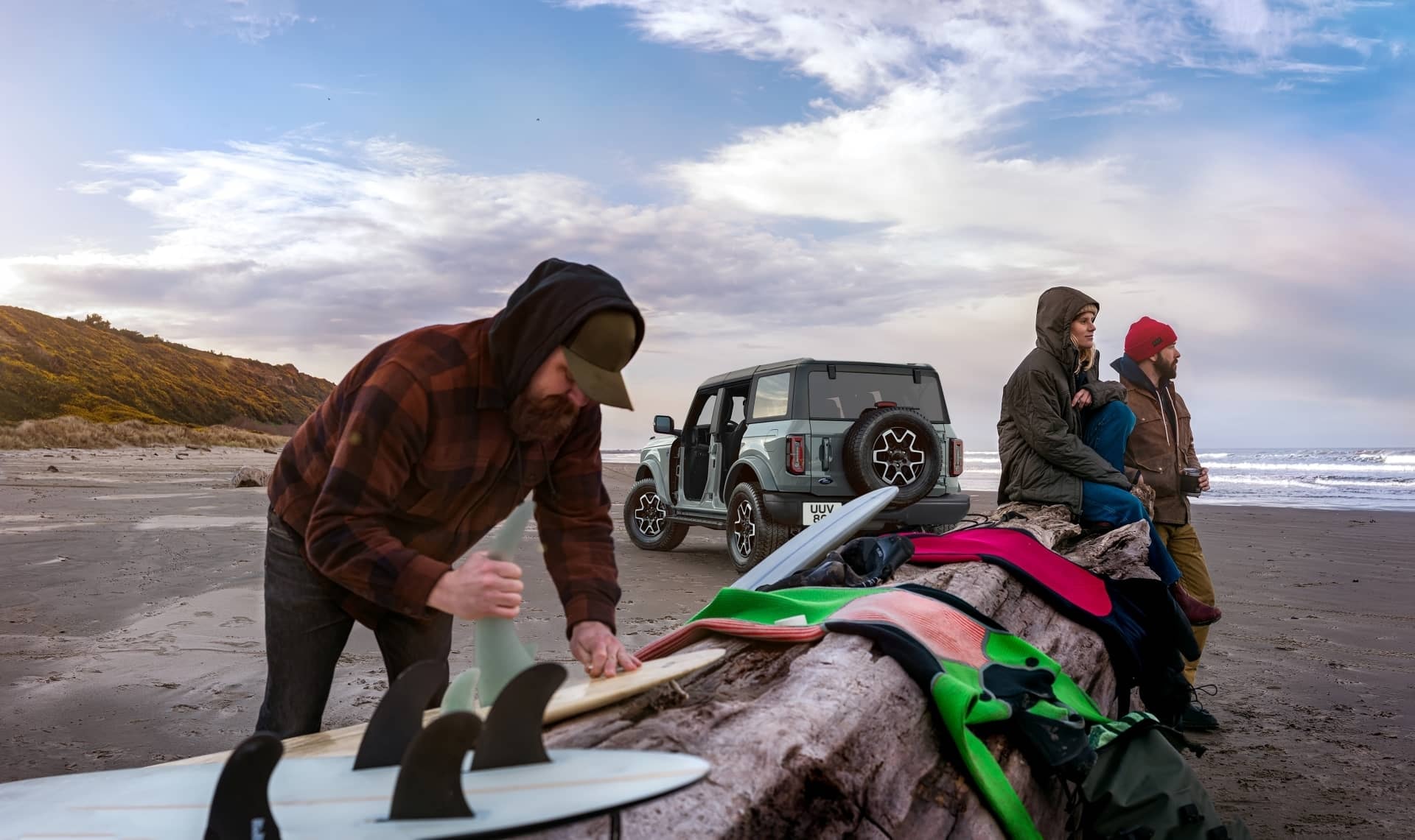 Grupos de personas preparándose para el surf con el Ford Bronco de fondo.