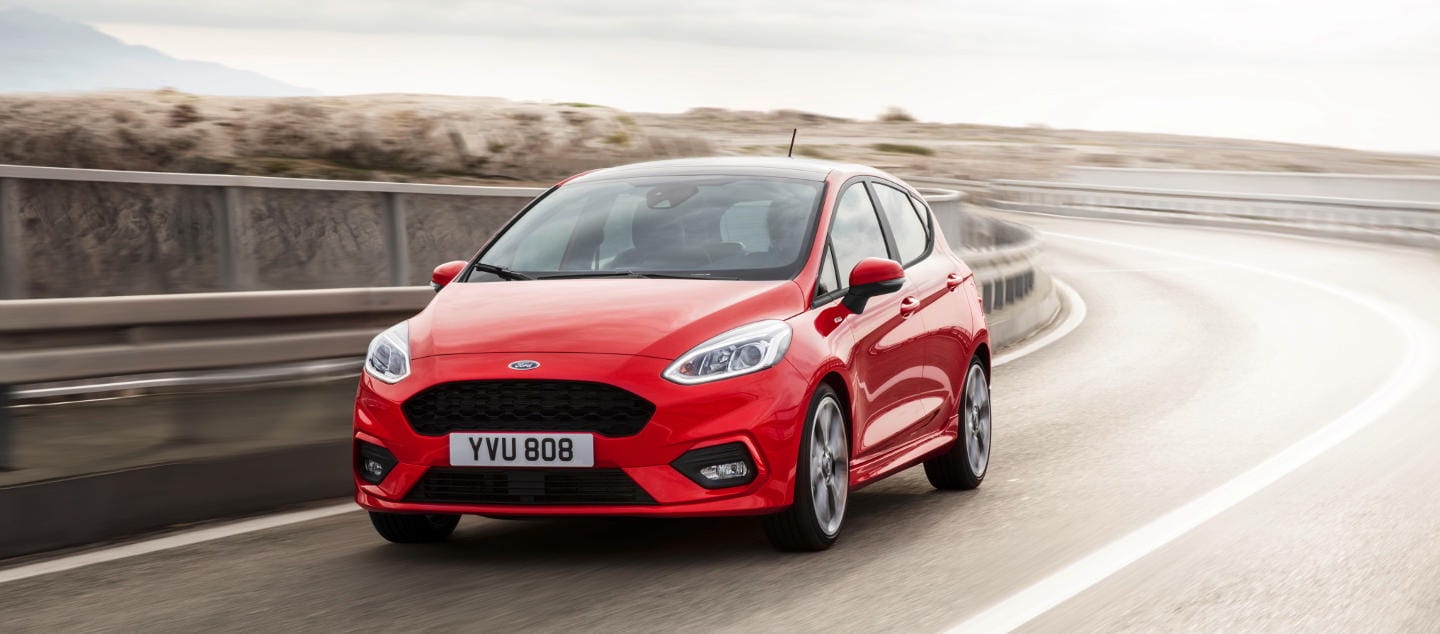 Ford Fiesta rojo capturado en trayecto, muestra frontal y lateral.