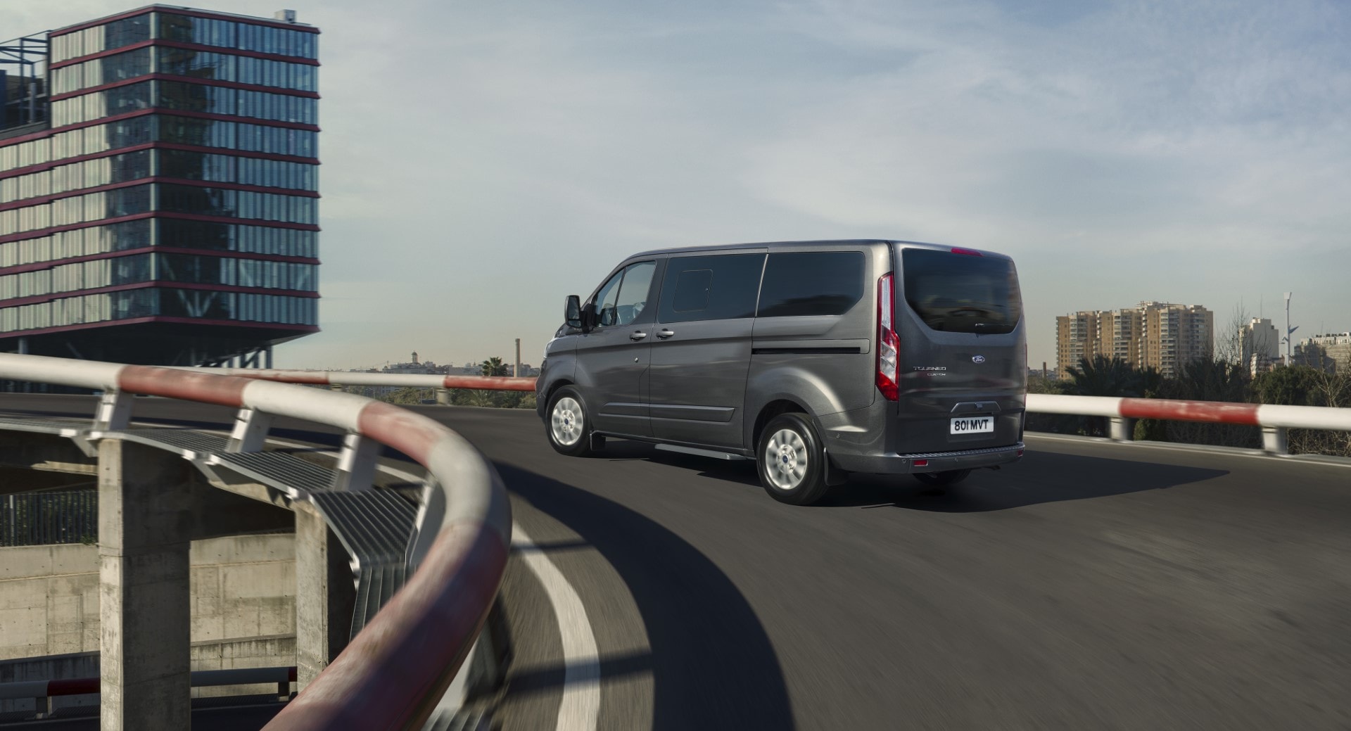 Imagen de la trasera y lateral del Ford Tourneo Custom en carretera urbana.