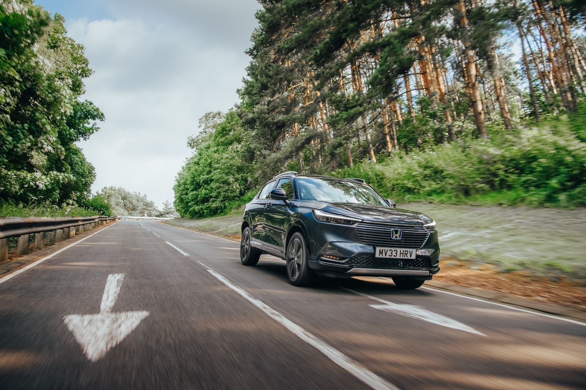 Vista frontal del Honda HR-V híbrido rodando por carretera arbolada.