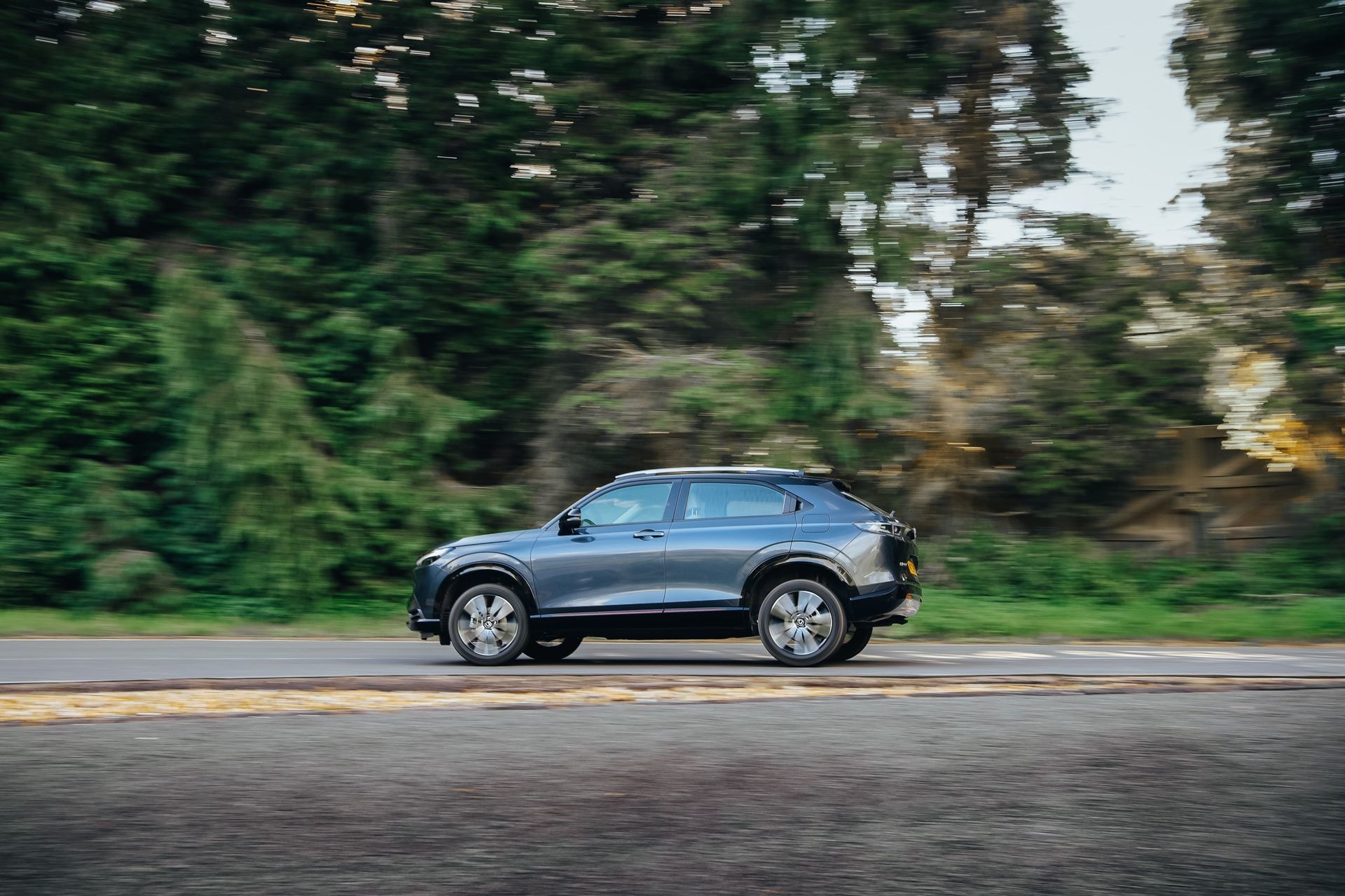 Perfil lateral del Honda HR-V híbrido en marcha, integrado con la naturaleza.