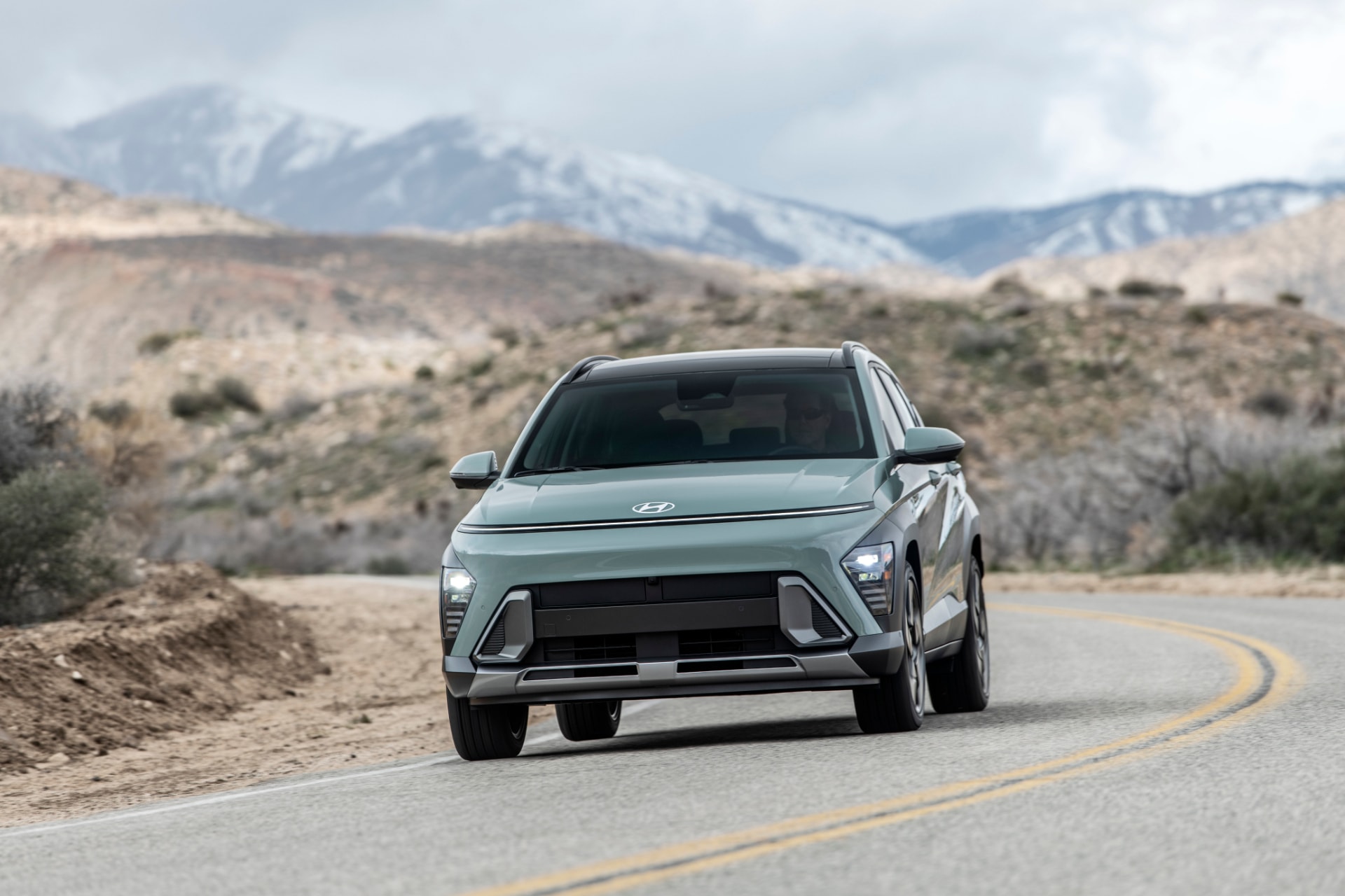 Vista frontal del Hyundai Kona Híbrido en carretera con paisaje montañoso.