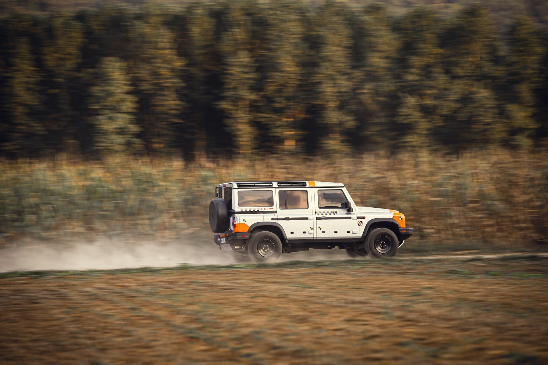 Perfil del Ineos Grenadier capturado en movimiento a través de un campo.