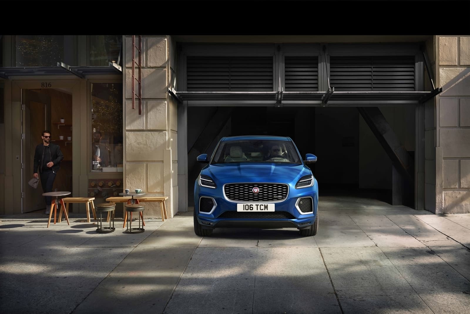 Un Jaguar E-Pace azul haciendo su aparición desde un moderno garaje urbano.