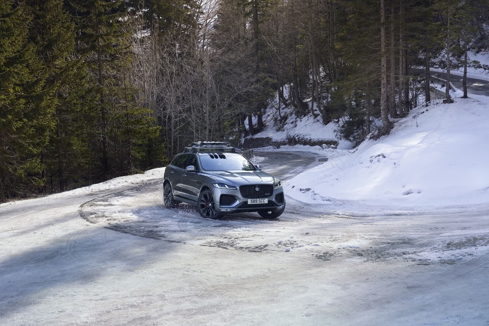 El F-Pace tomando una curva nevada, destacando su perfil trasero y diseño deportivo.