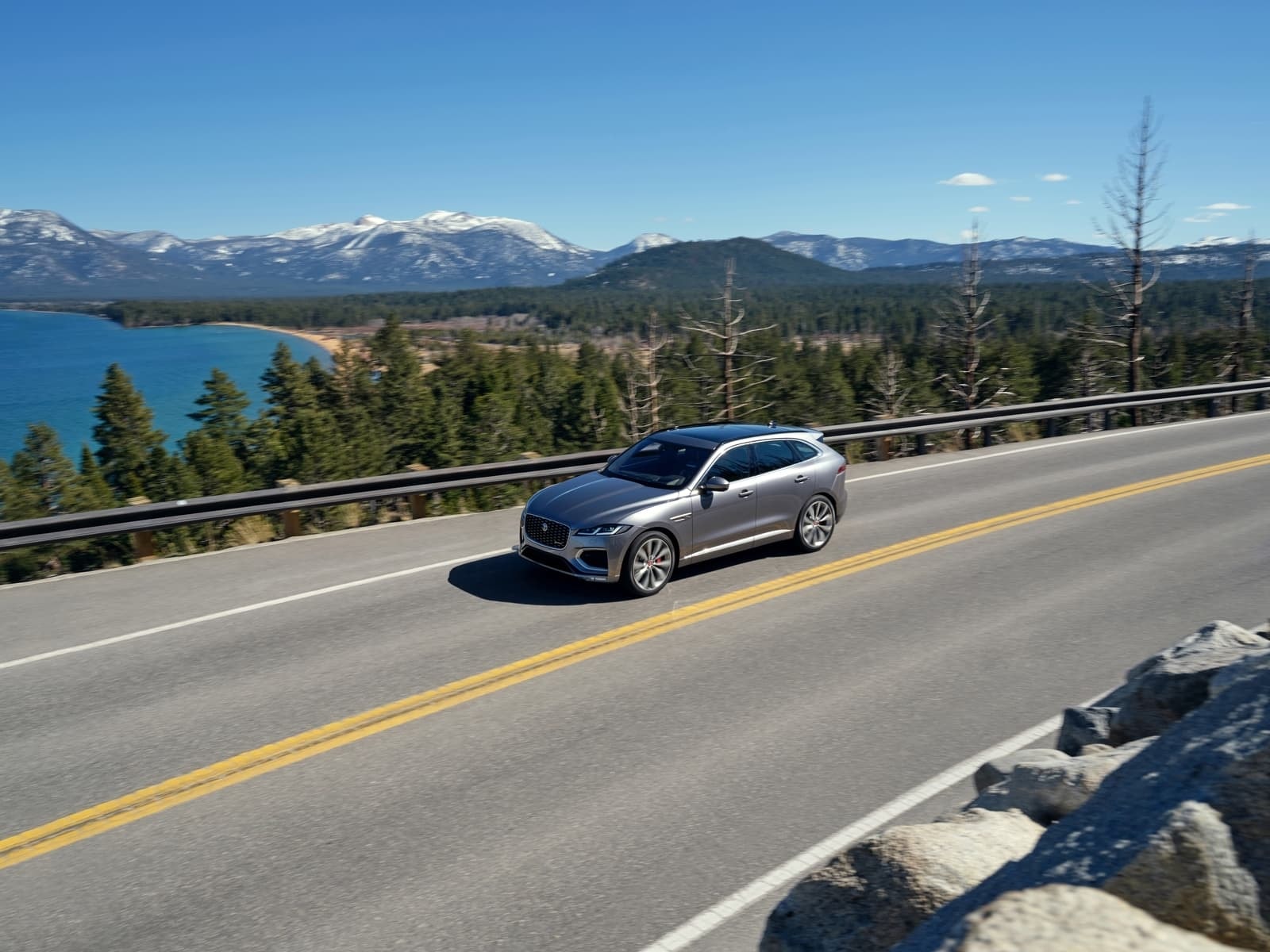 Captura del Jaguar F-Pace en perfil lateral sobre una carretera con vistas al lago.