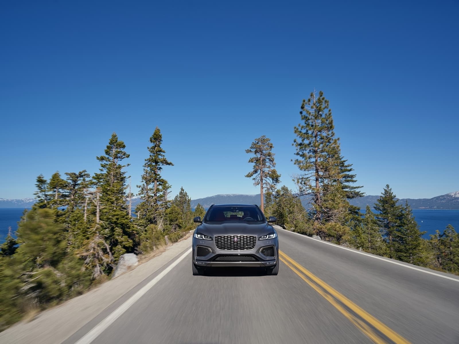 Imponente toma frontal del Jaguar F-Pace en una vía con vistas al lago.