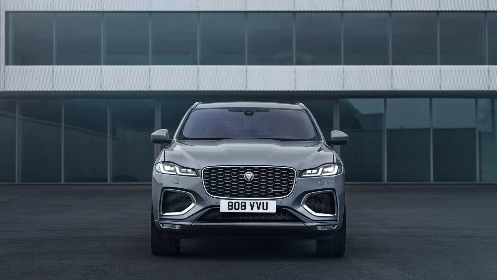 F-Pace frente a fachada moderna, enfatizando su diseño frontal y modernidad.