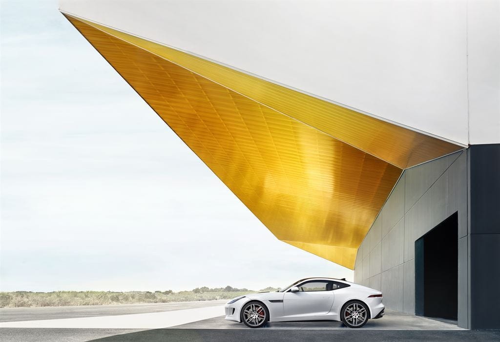 El Jaguar F-Type Coupé blanco posa junto a una estructura arquitectónica moderna.