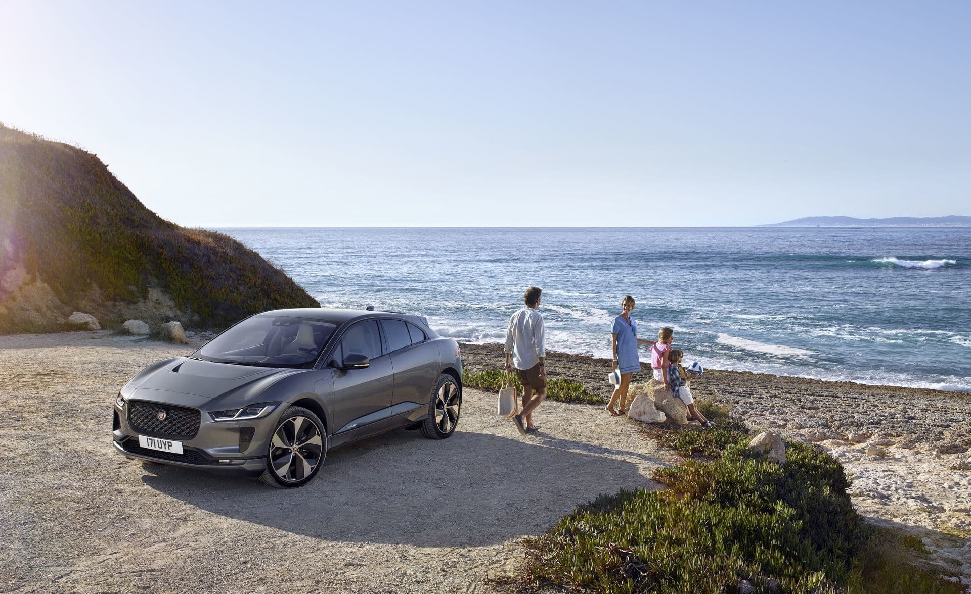 Familia caminando hacia su Jaguar I-Pace con el mar de fondo.