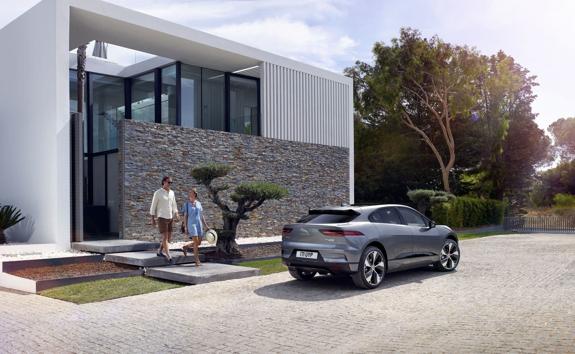 Vista lateral del Jaguar I-Pace junto a una familia y su hogar contemporáneo.