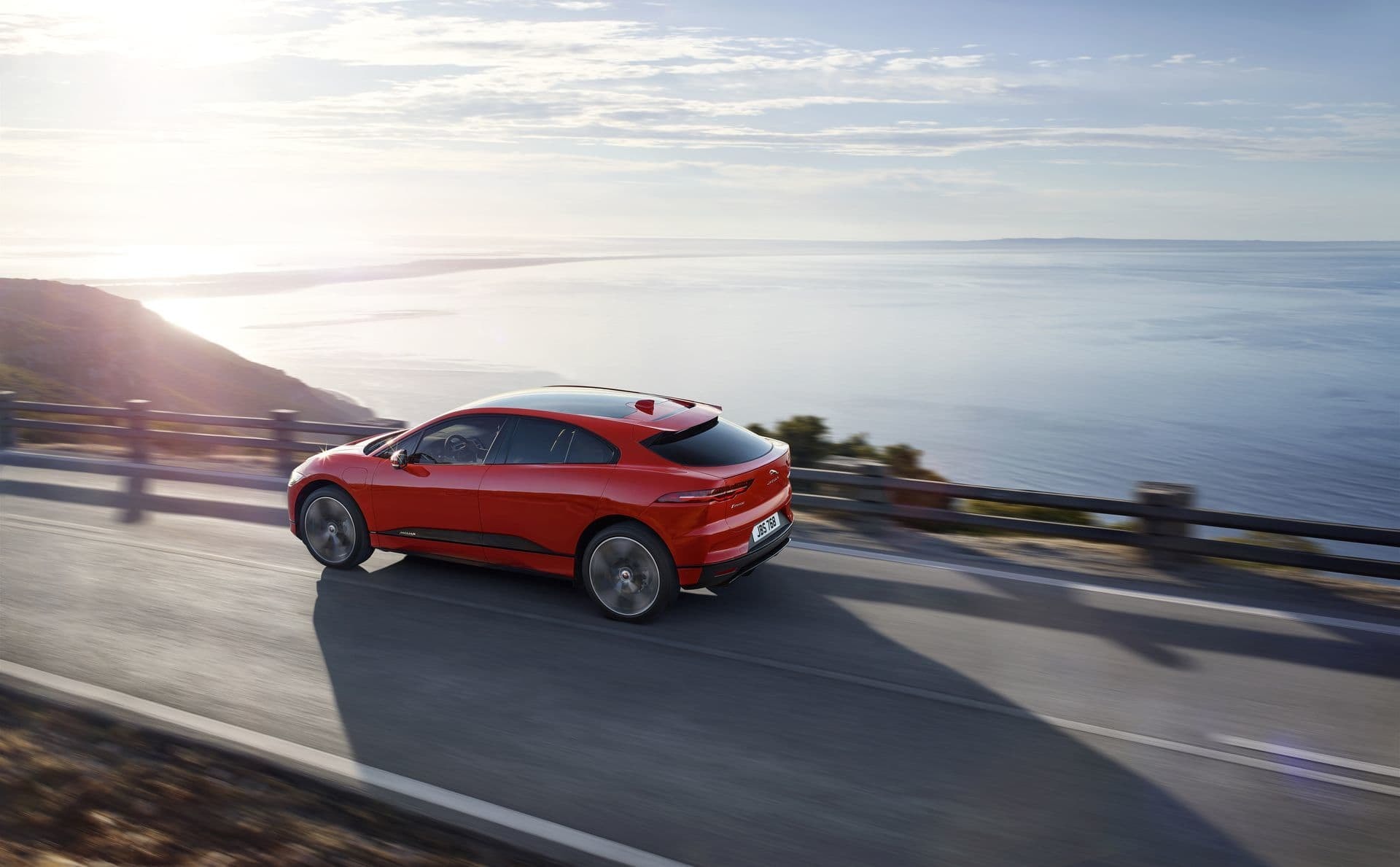 Vista trasera del Jaguar I-Pace en carretera con paisaje de costa al fondo.
