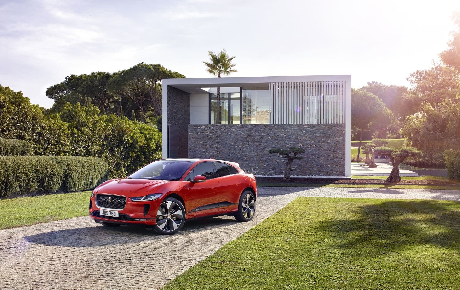 Jaguar I-Pace rojo delante de una residencia moderna, enfatizando su diseño frontal.