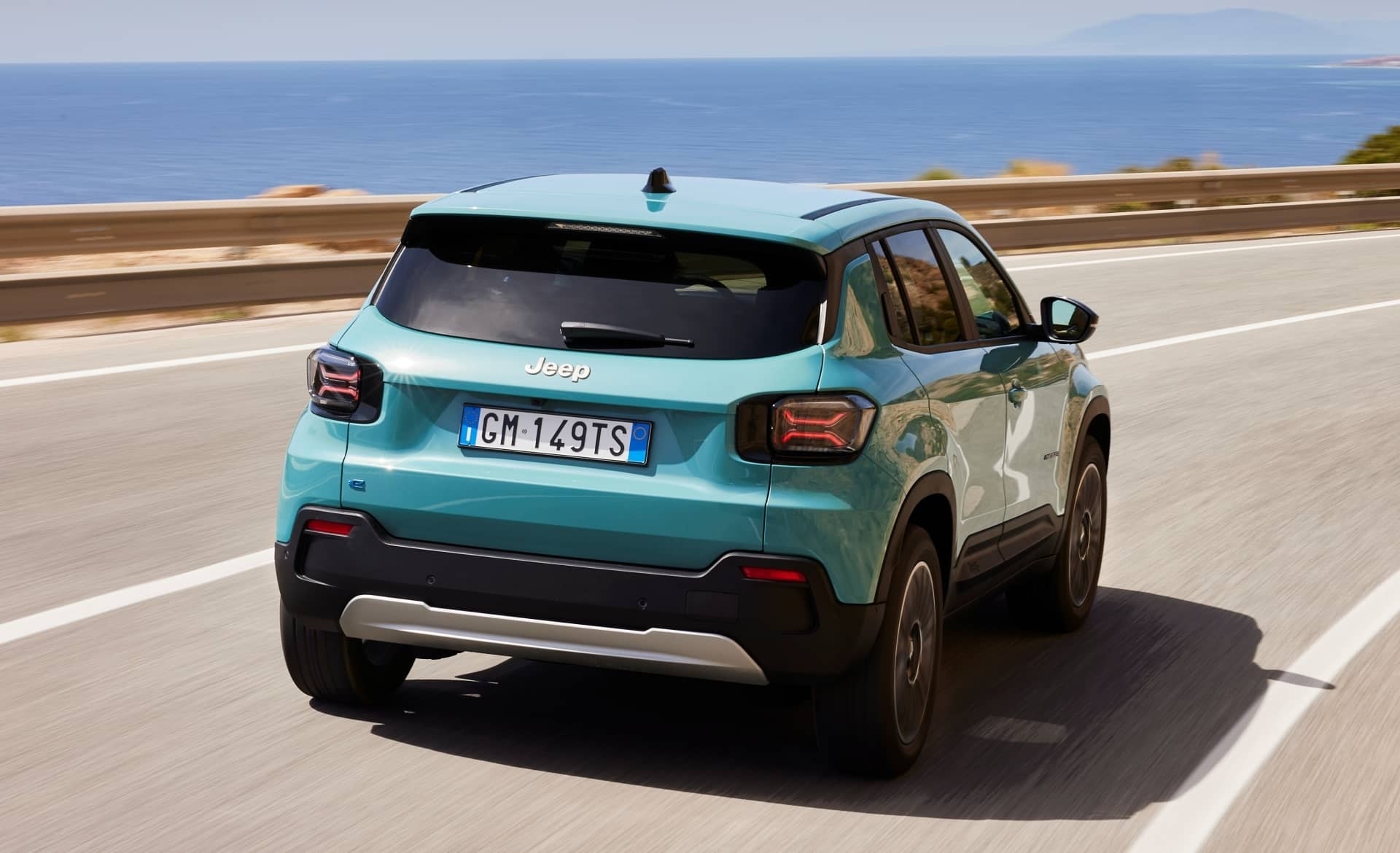 Jeep Avenger en color turquesa rodando por carretera, vista trasera y lateral.