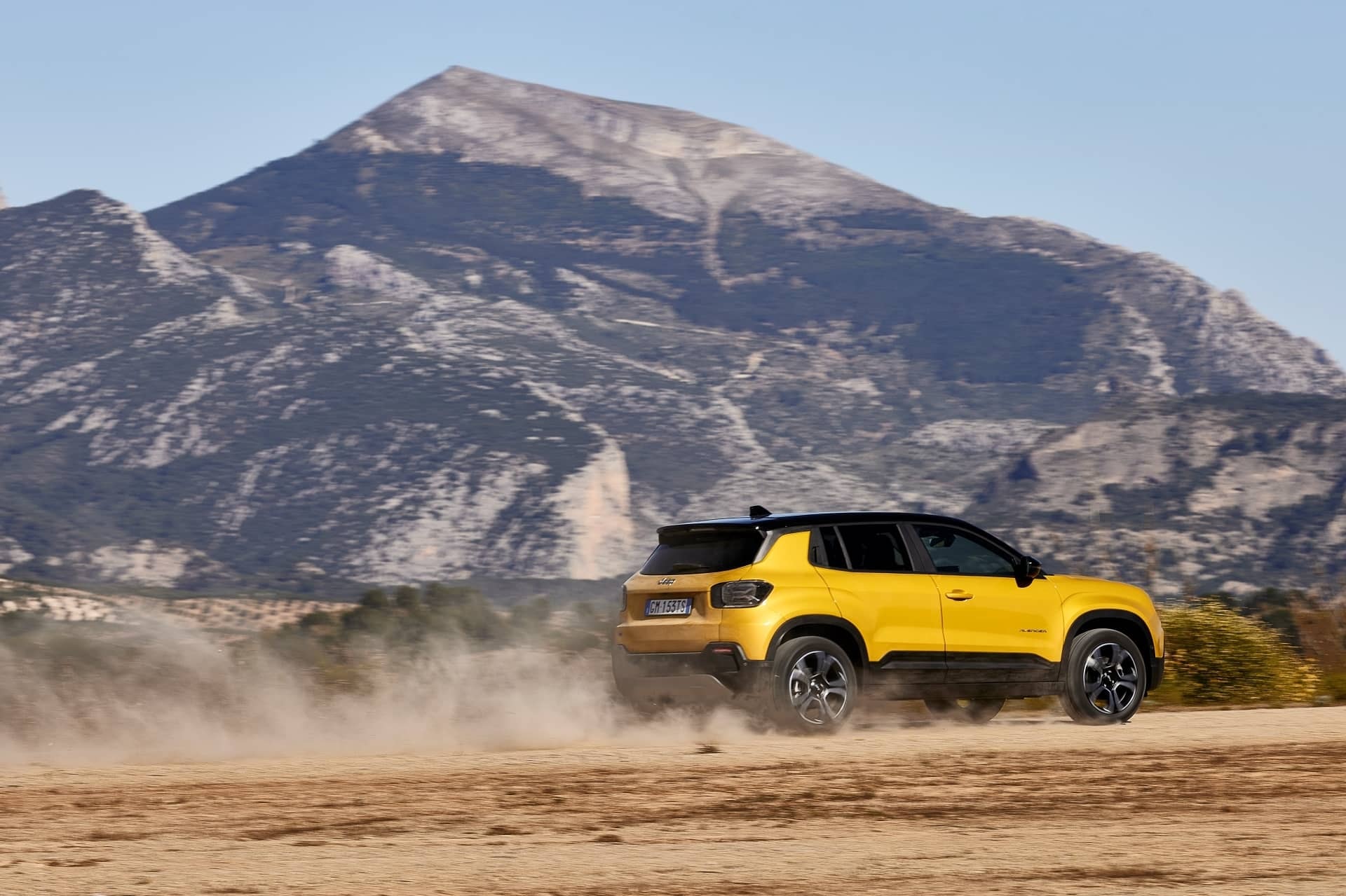 Jeep Avenger superando terreno arenoso con montaña de fondo.