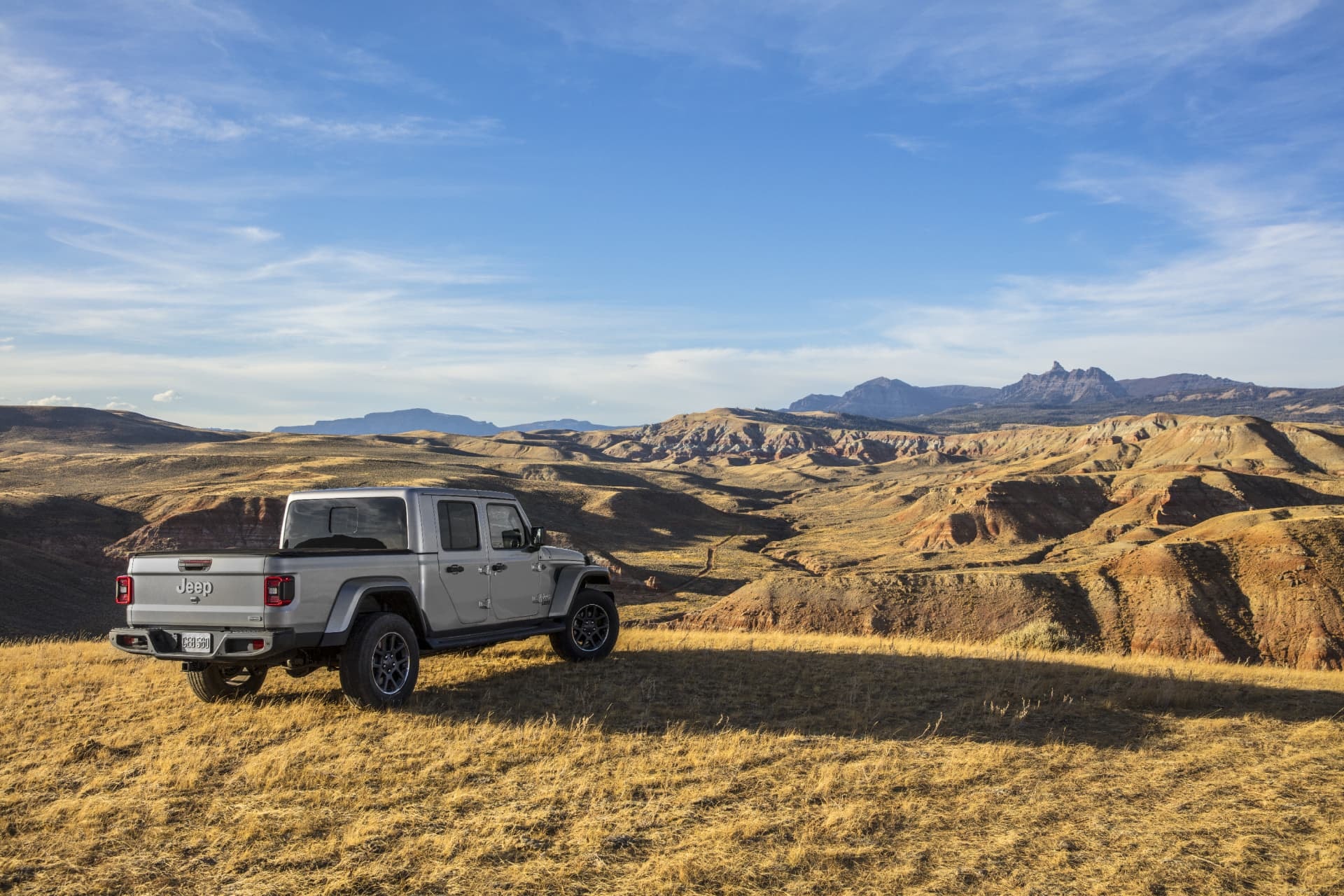 Imagen trasera y lateral de un Jeep Gladiator blanco en un paisaje de montaña.
