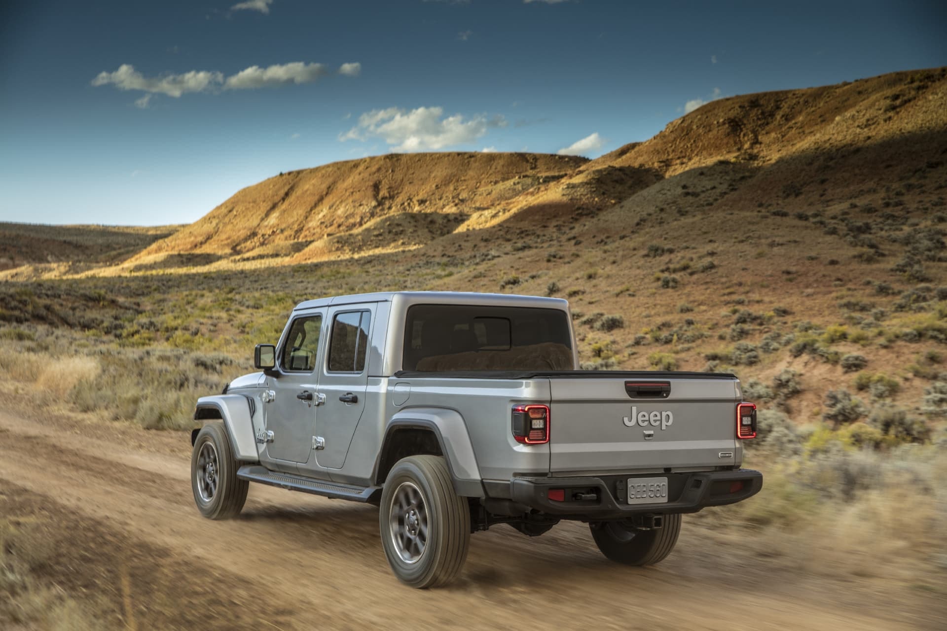 Jeep Gladiator gris mostrando su trasera y lateral en un paisaje desértico.