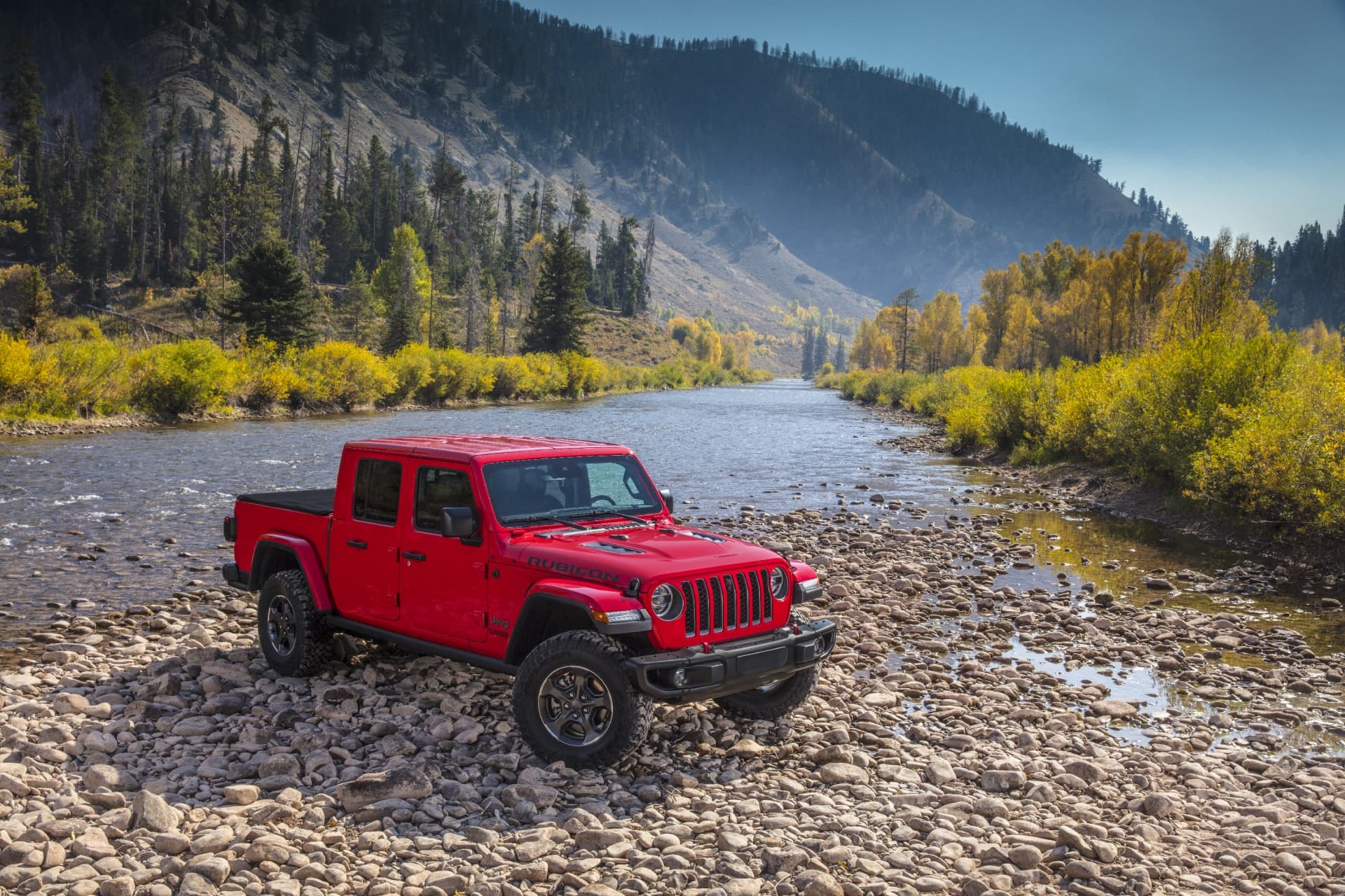 Jeep Gladiator en rojo, junto a un río y vegetación otoñal, en perfecta armonía con la aventura.