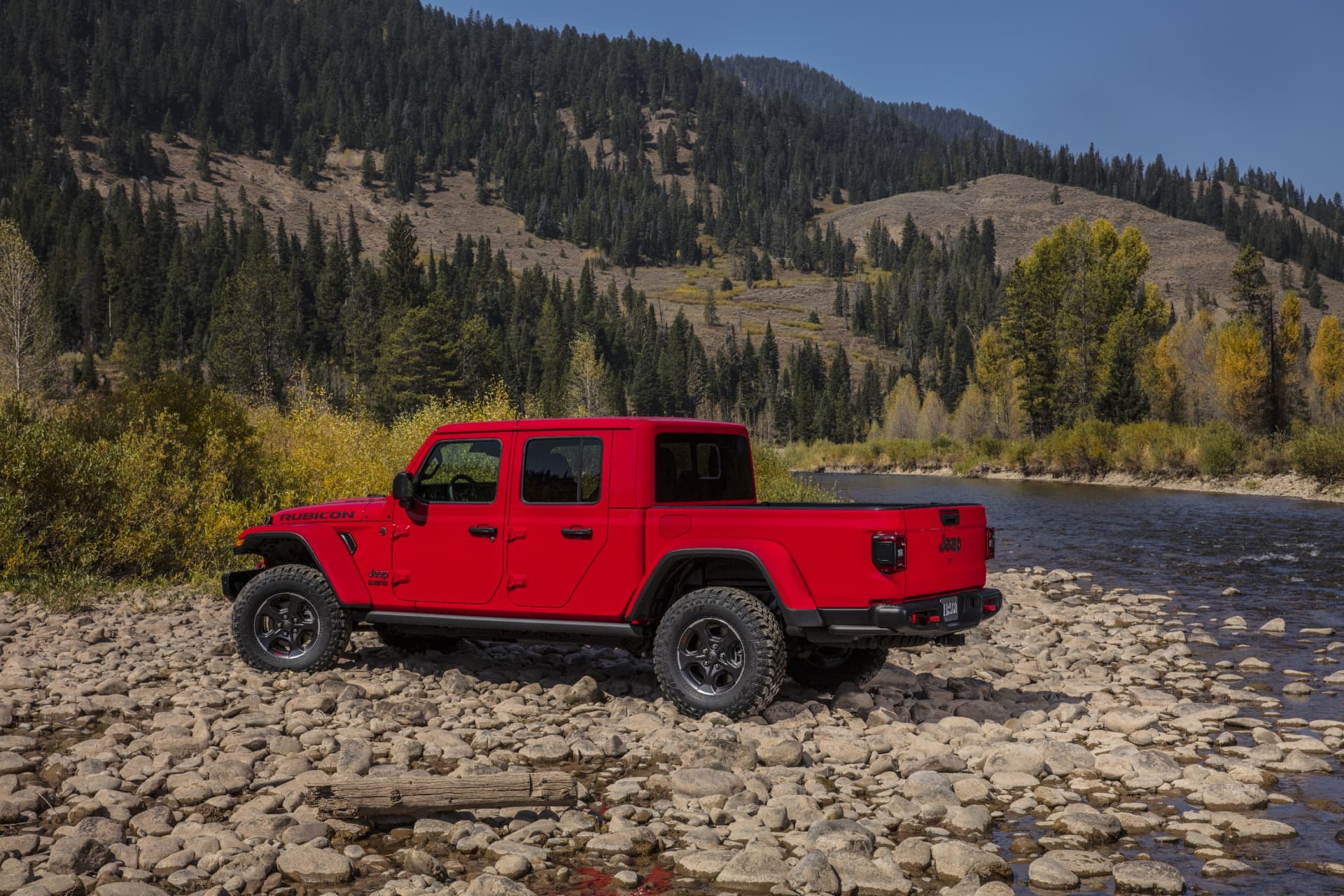 Jeep Gladiator color rojo estacionado cerca de un río, mostrando su atractivo diseño y funcionalidad.