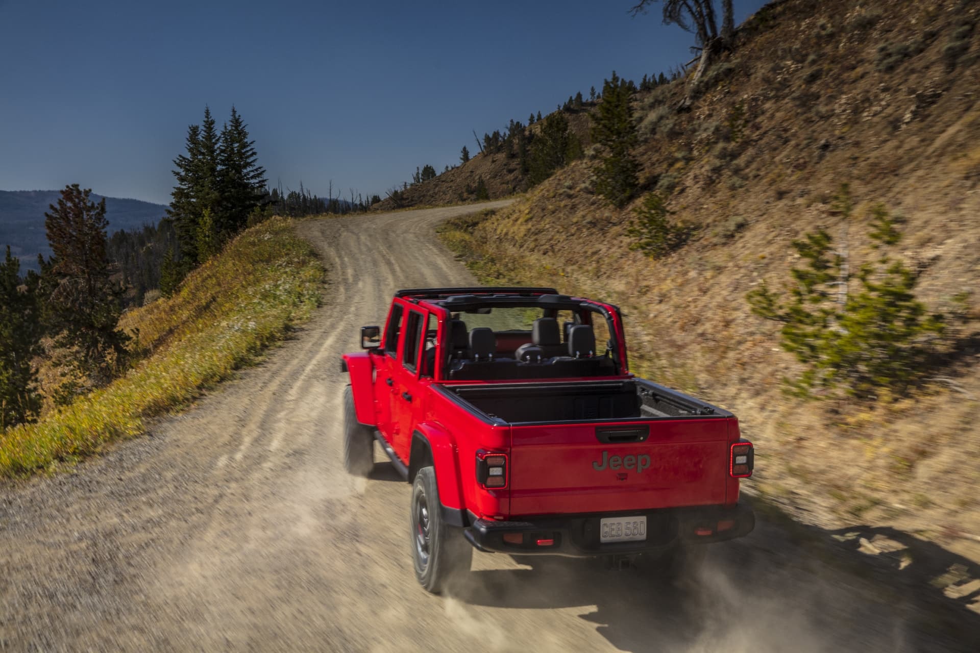 Parte trasera de un Jeep Gladiator rojo acelerando en una pista de tierra.