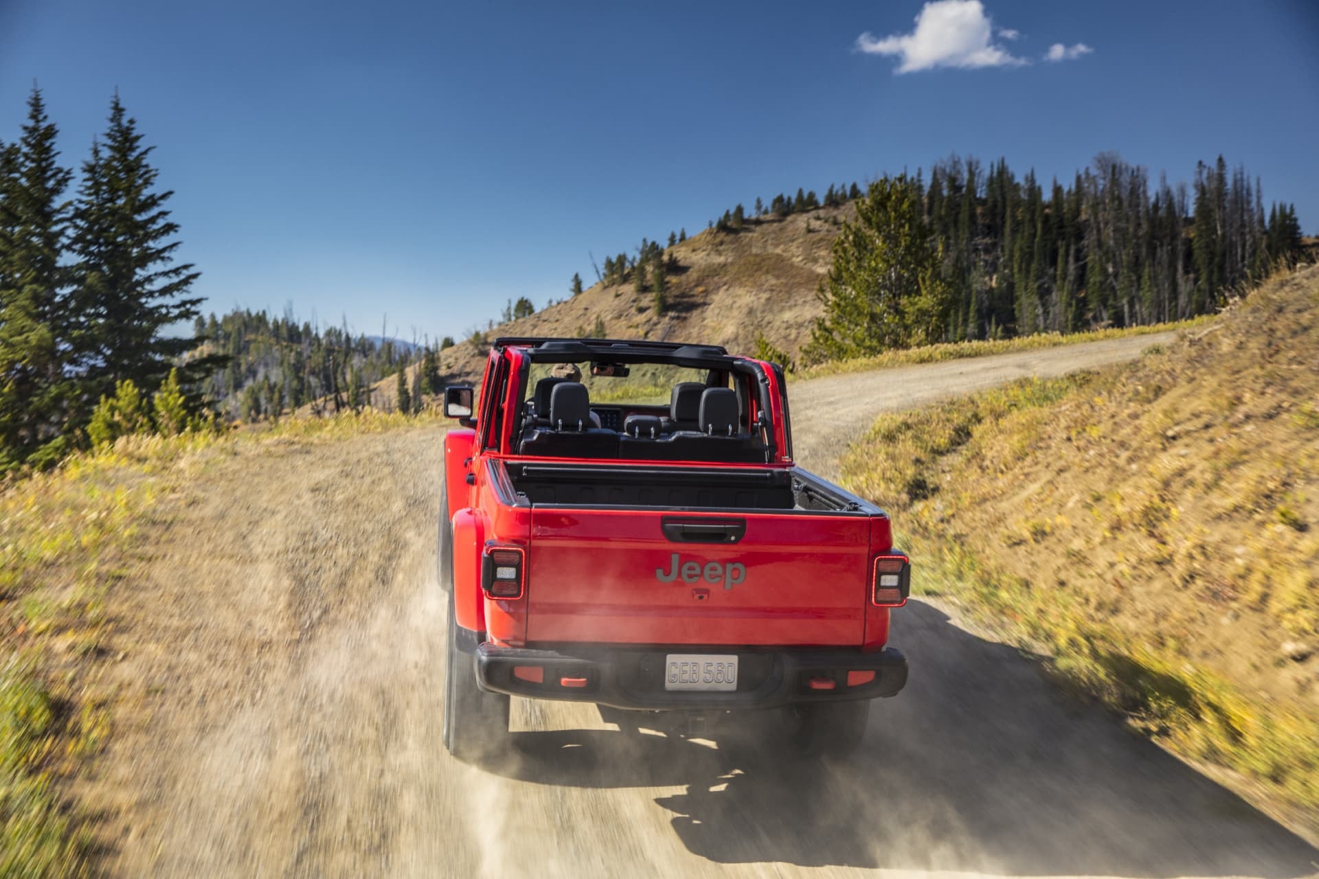 Vista trasera del Jeep Gladiator rojo en acción en una pista de tierra rural.