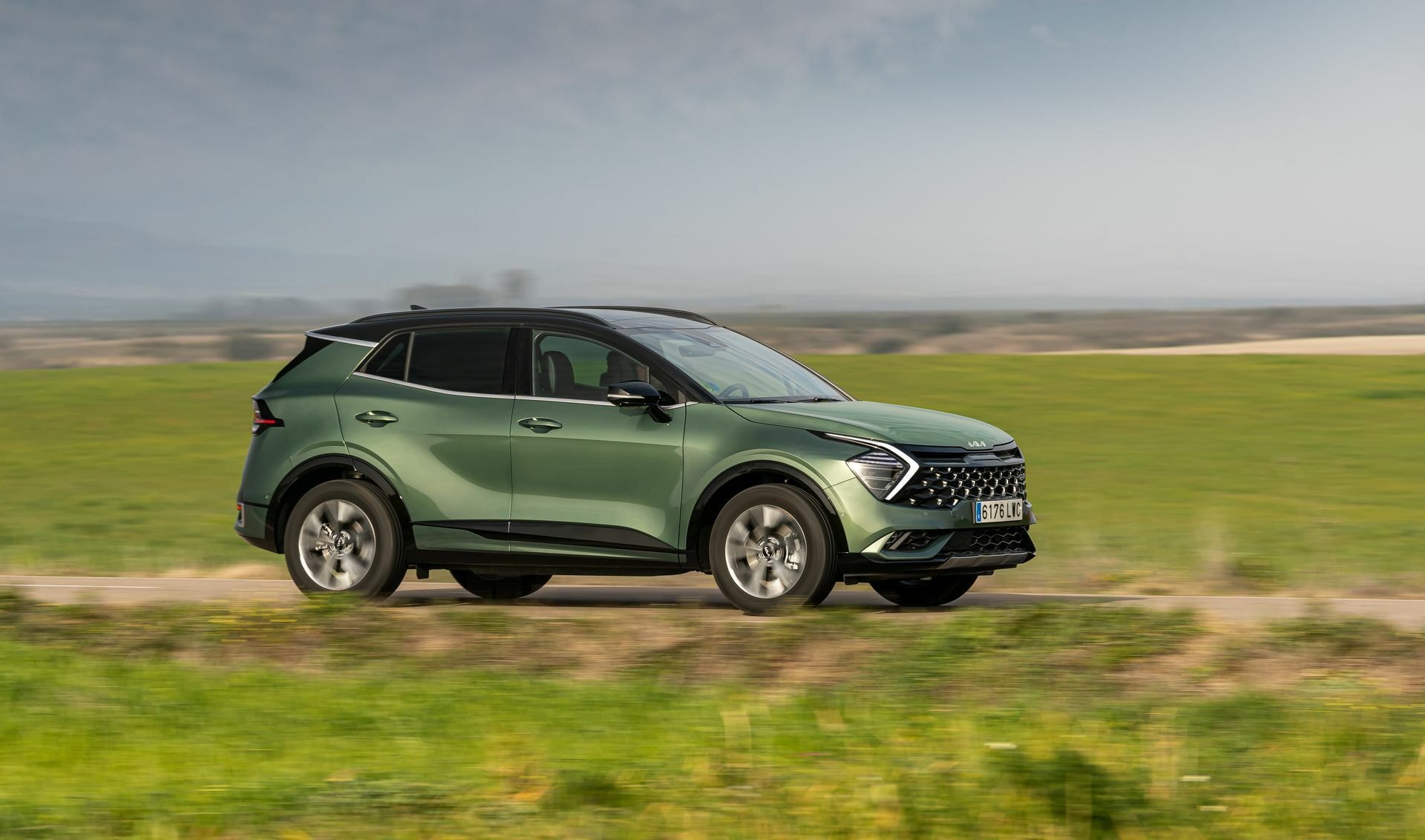 Vista lateral del Kia Sportage en movimiento por carretera rural