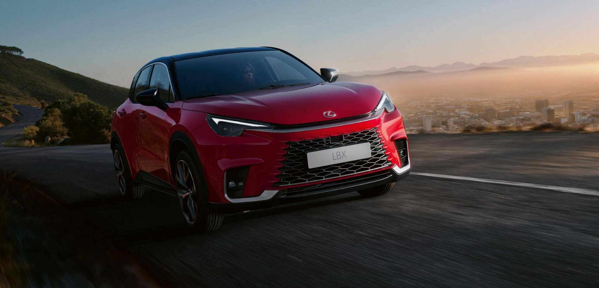 Dynamic view of a Lexus LBX driving at dawn, highlighting the car's road presence and sleek design.