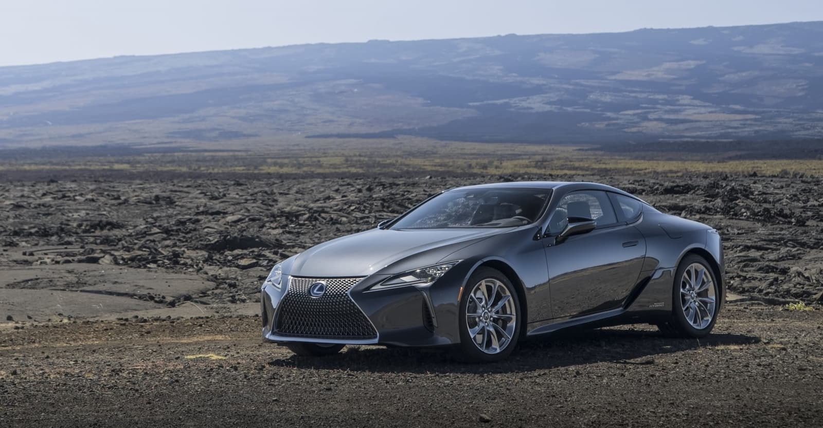 Lexus LC híbrido aparcado en paisaje natural, mostrando su diseño en armonía con el entorno.